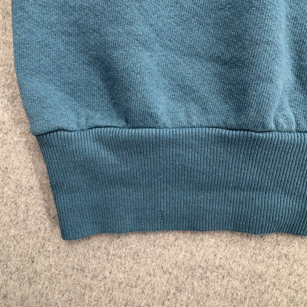 Close-up of a blue fabric edge on a beige surface. bottom hem has small hole
