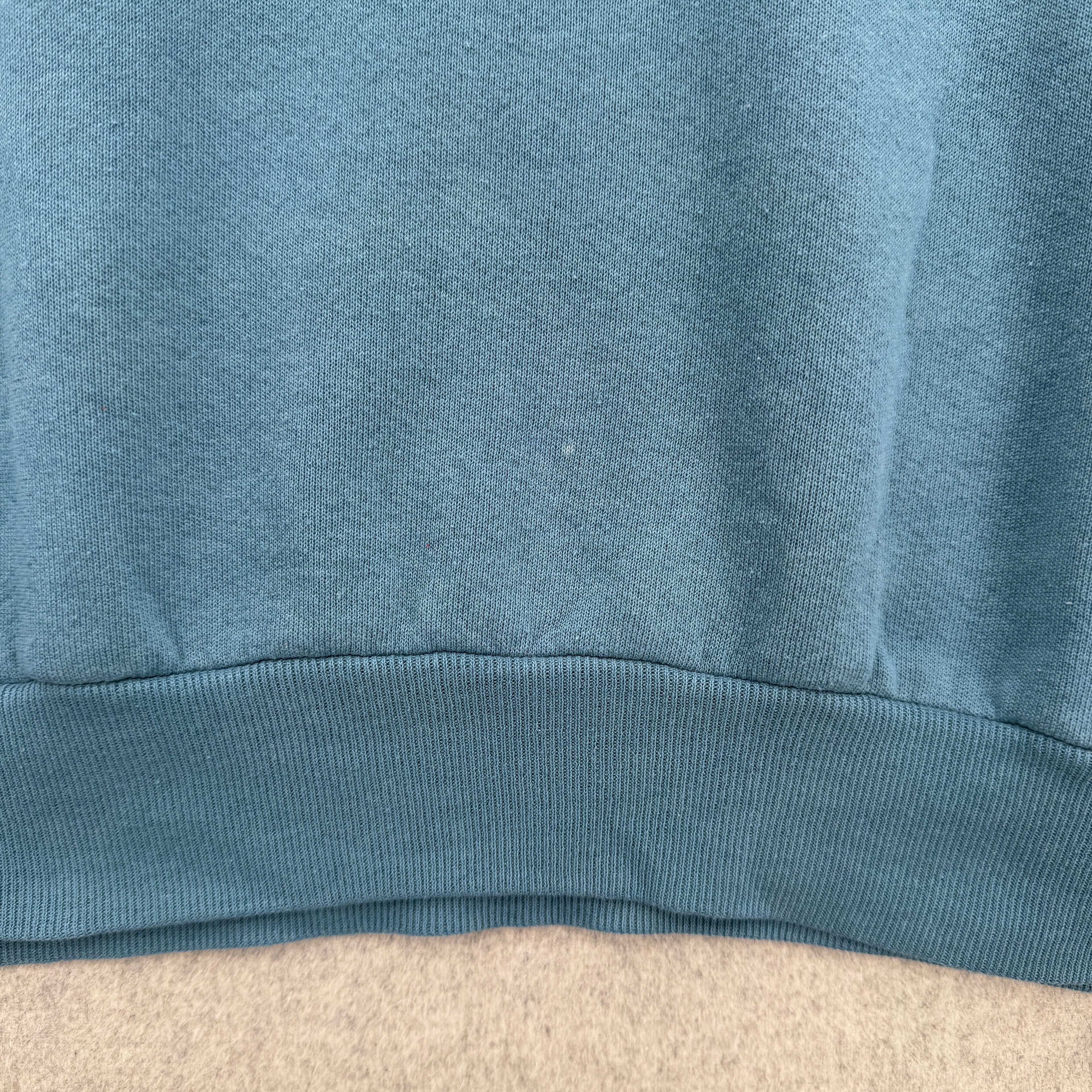 Close-up of a blue fabric texture on a beige surface. bottom of sweatshirt has some light faint stain spots