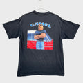 Black t-shirt with a graphic design on a gray surface. Camel Cigaretts logo with a camel character hands crossed standing in front of a vintage car