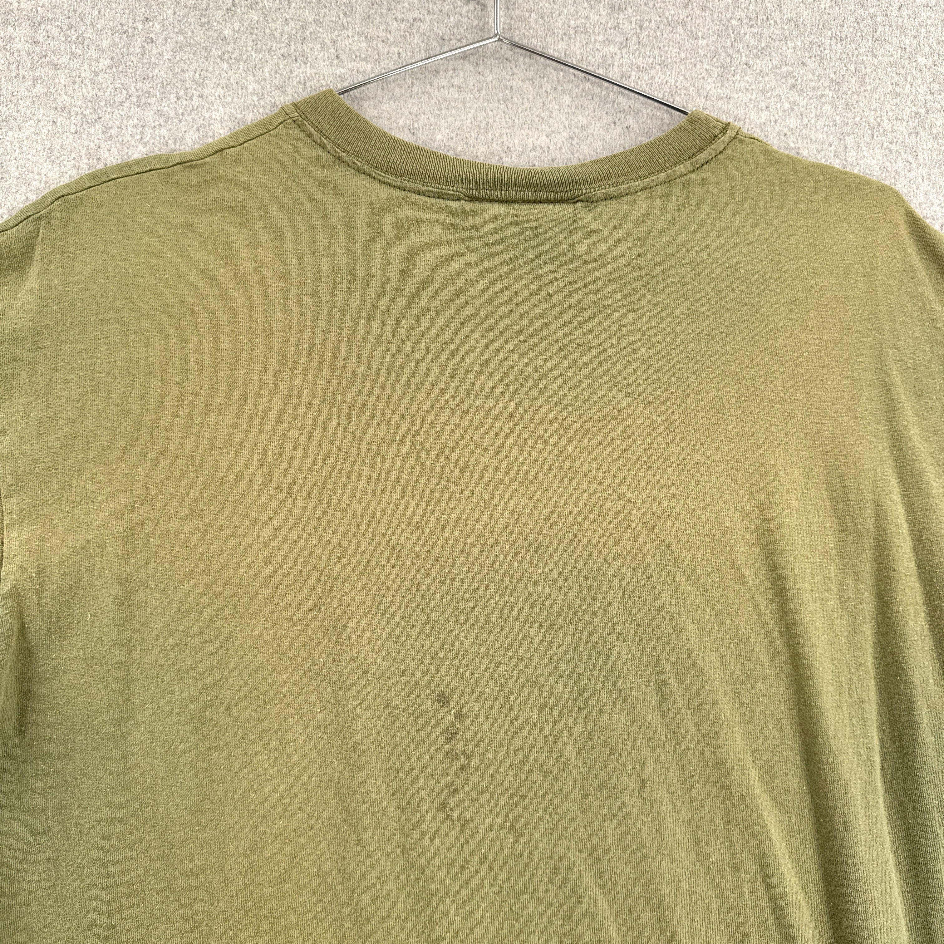 Green t-shirt on a hanger with a visible stain on the back
