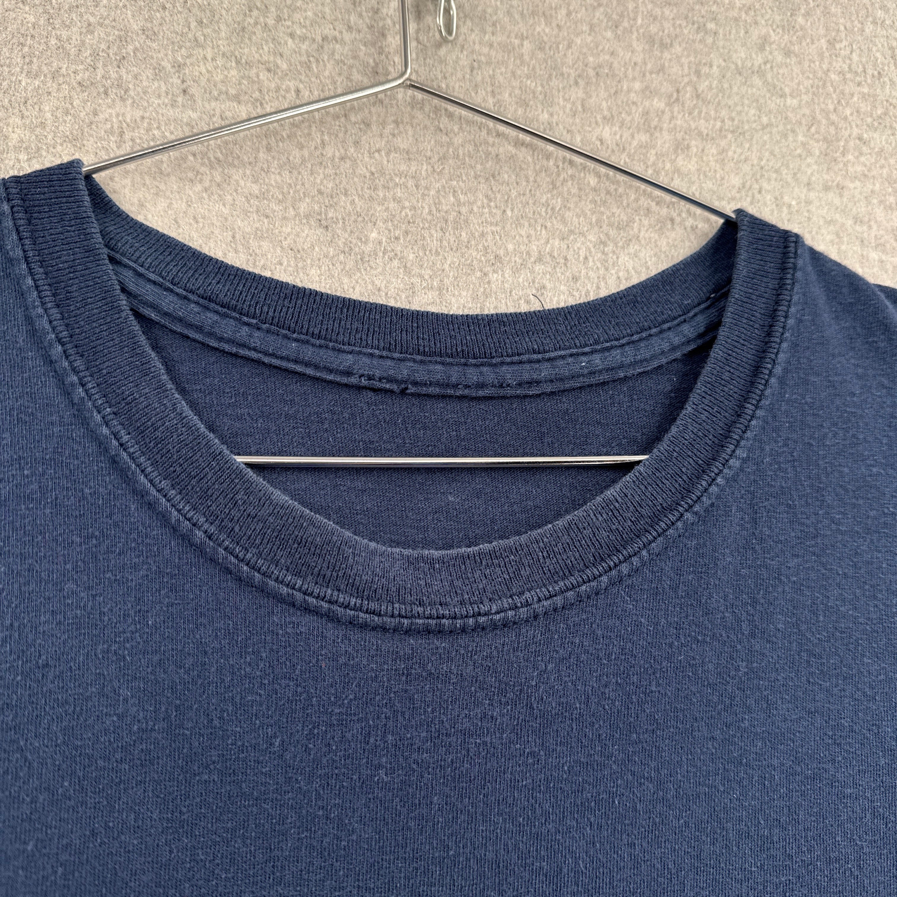 Navy blue t-shirt on a hanger against a beige wall. No tag