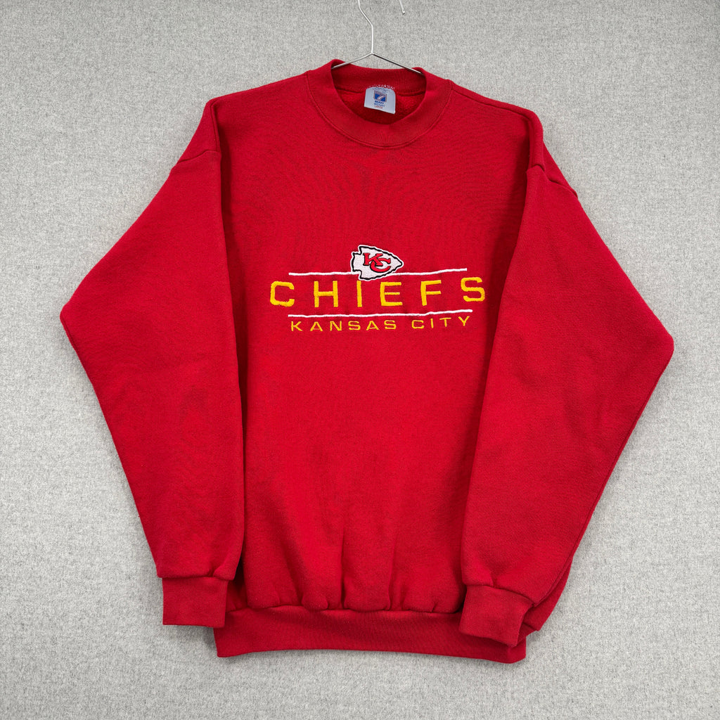 Red sweatshirt with 'Chiefs Kansas City' text and logo on a gray background. Sleeves folded over