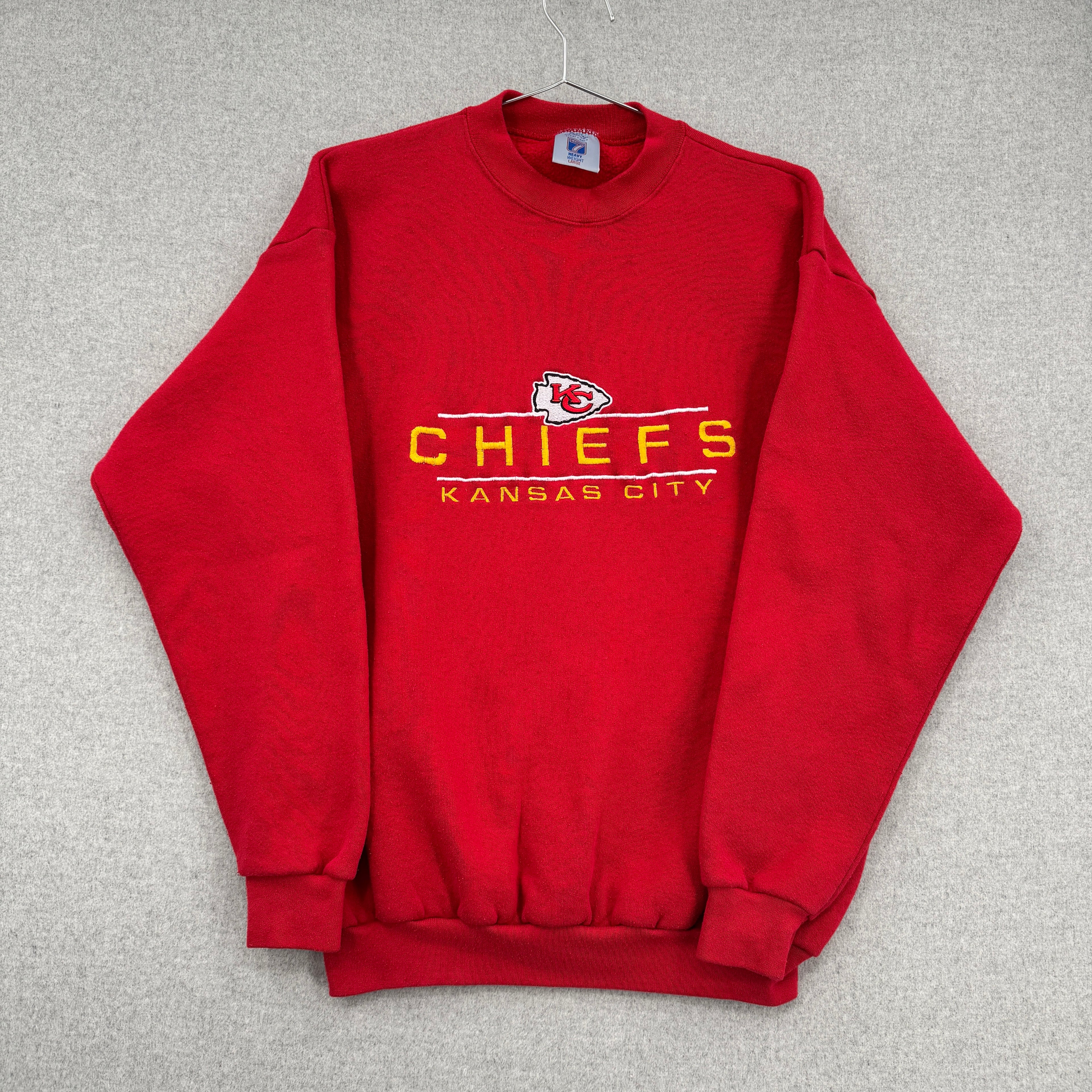 Red sweatshirt with 'Chiefs Kansas City' text and logo on a gray background. Sleeves folded over