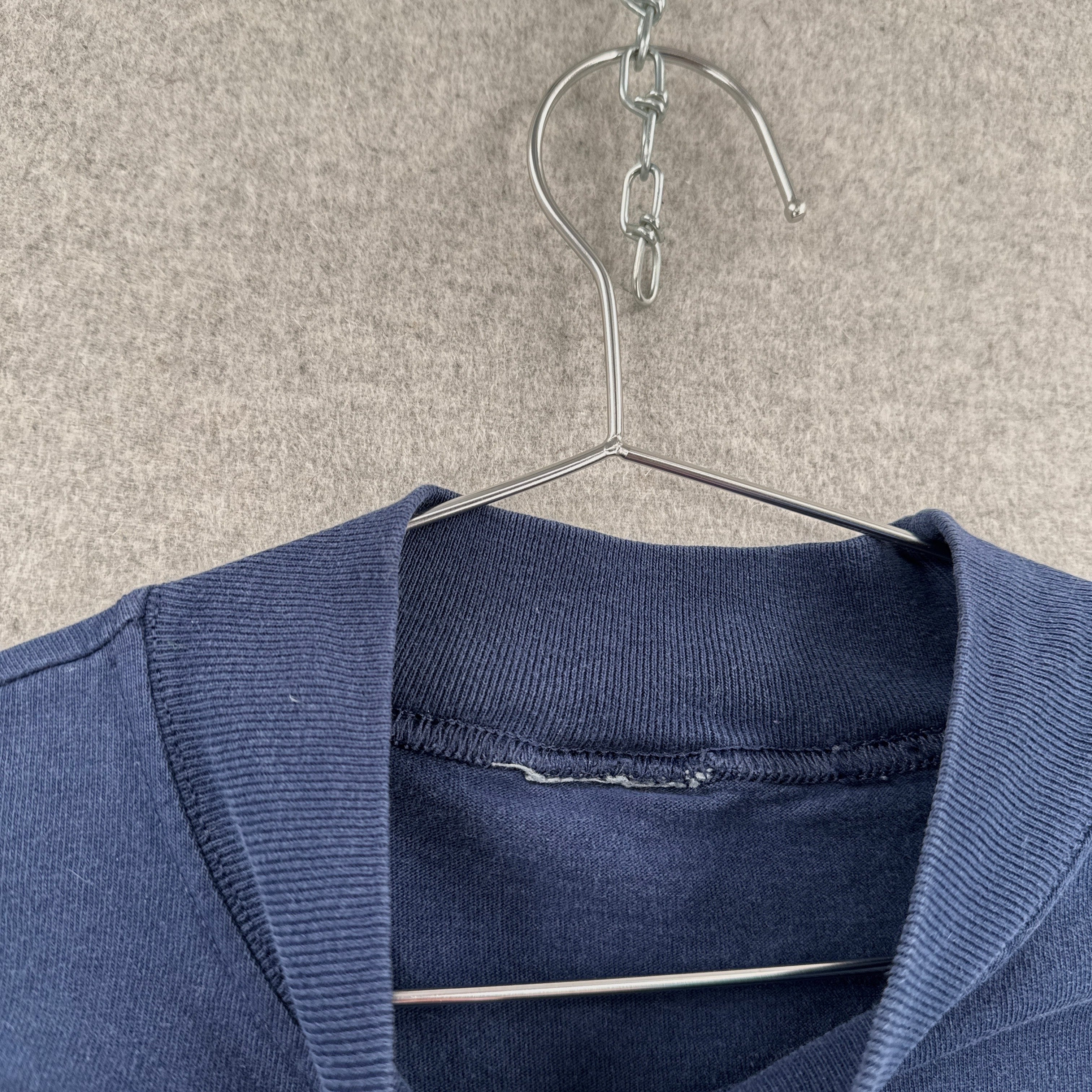 Blue sweater on a metal hanger against a beige background. tag missing