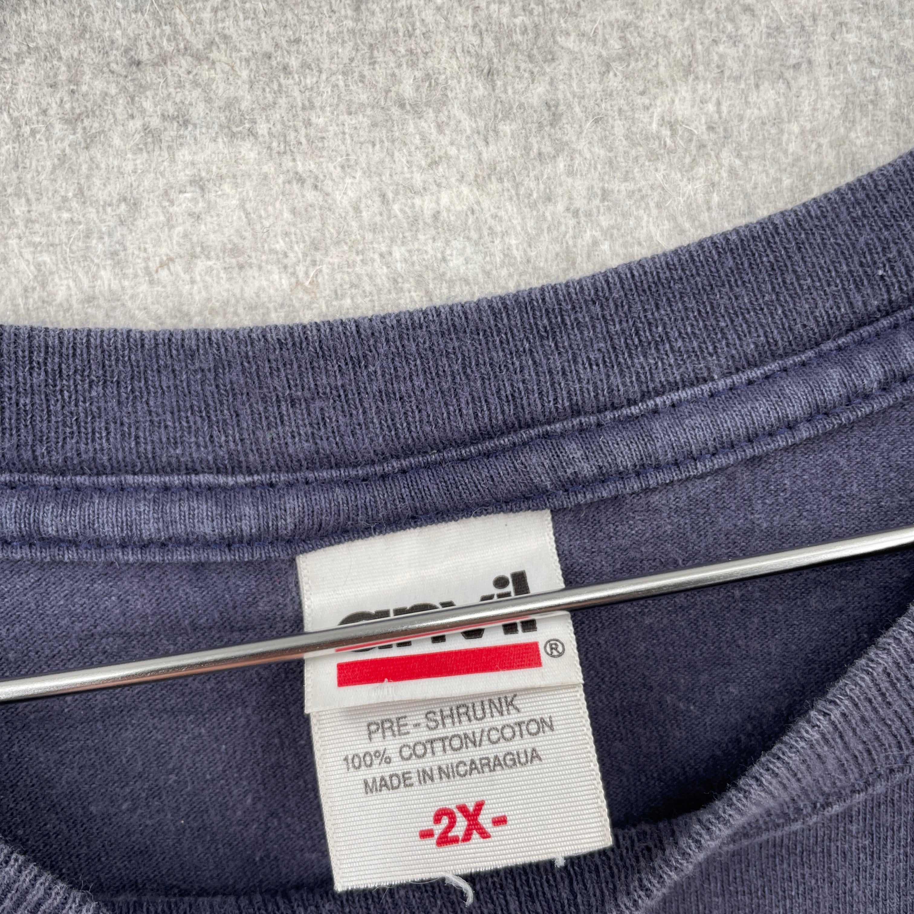 Close-up of a fabric label on a garment with text and symbols. Anvil tag 100% cotton made in Nicaragua size 2XL