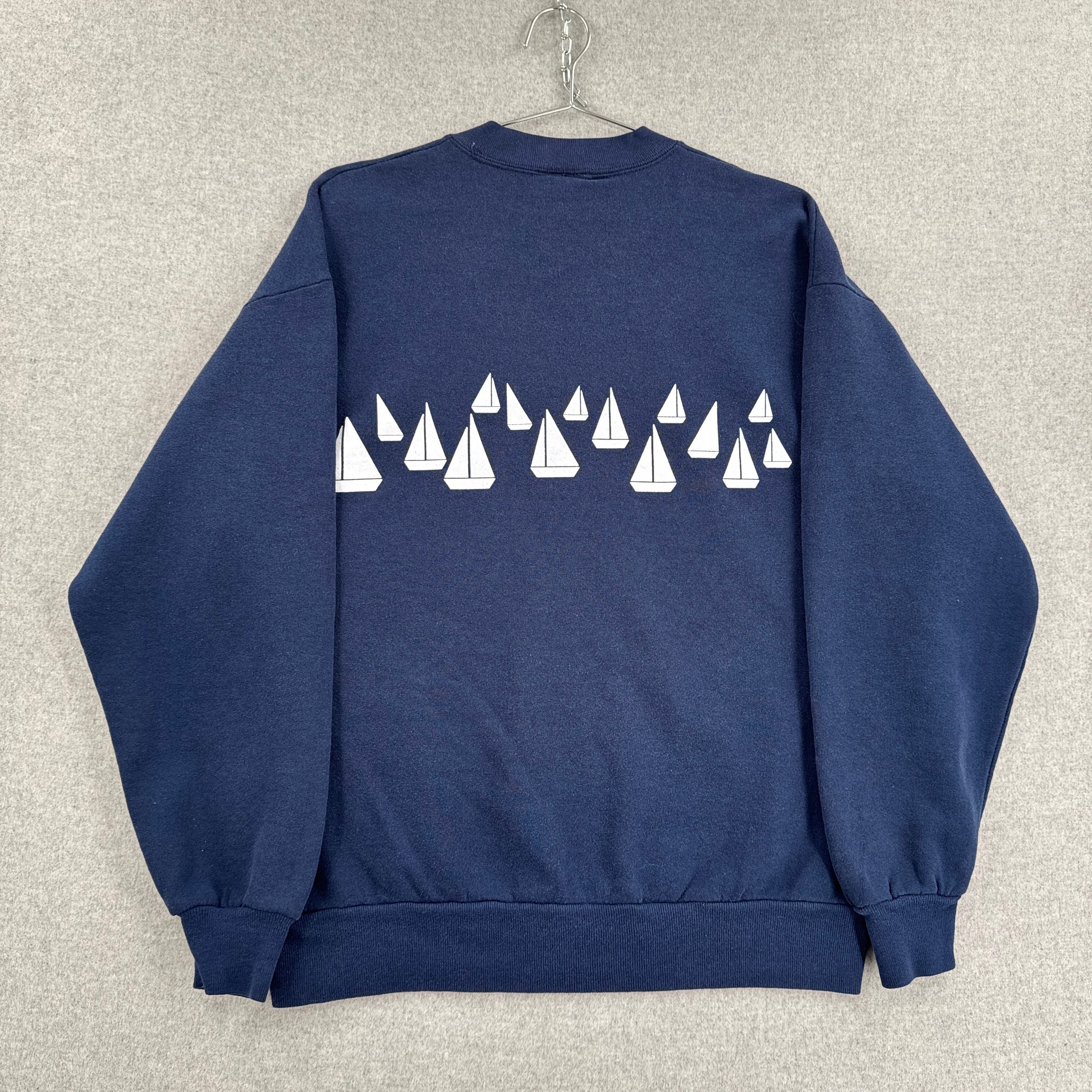 Navy blue sweatshirt with white sailboat pattern on a textured gray background