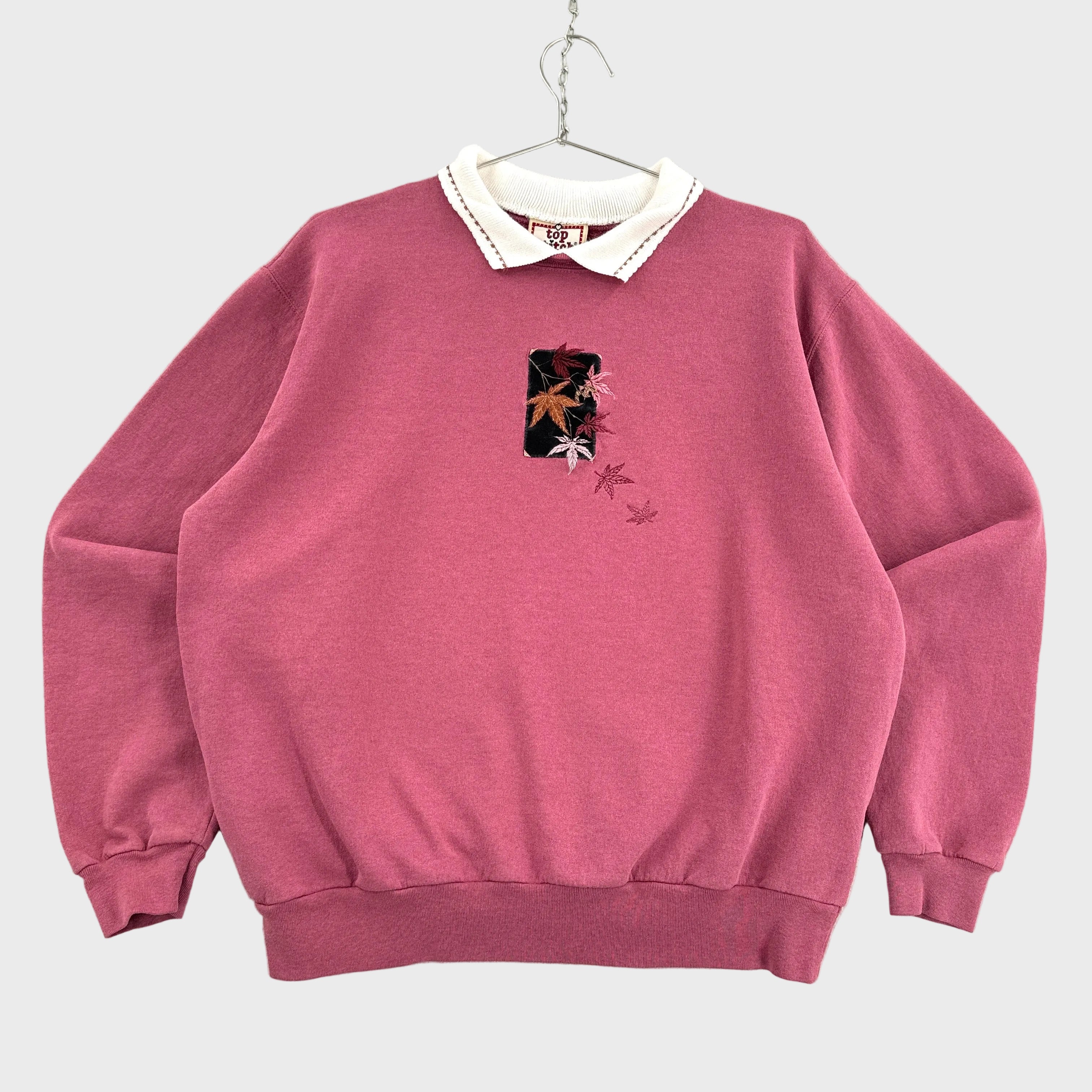 Pink sweatshirt with a small fall leaves graphic on a gray textured background