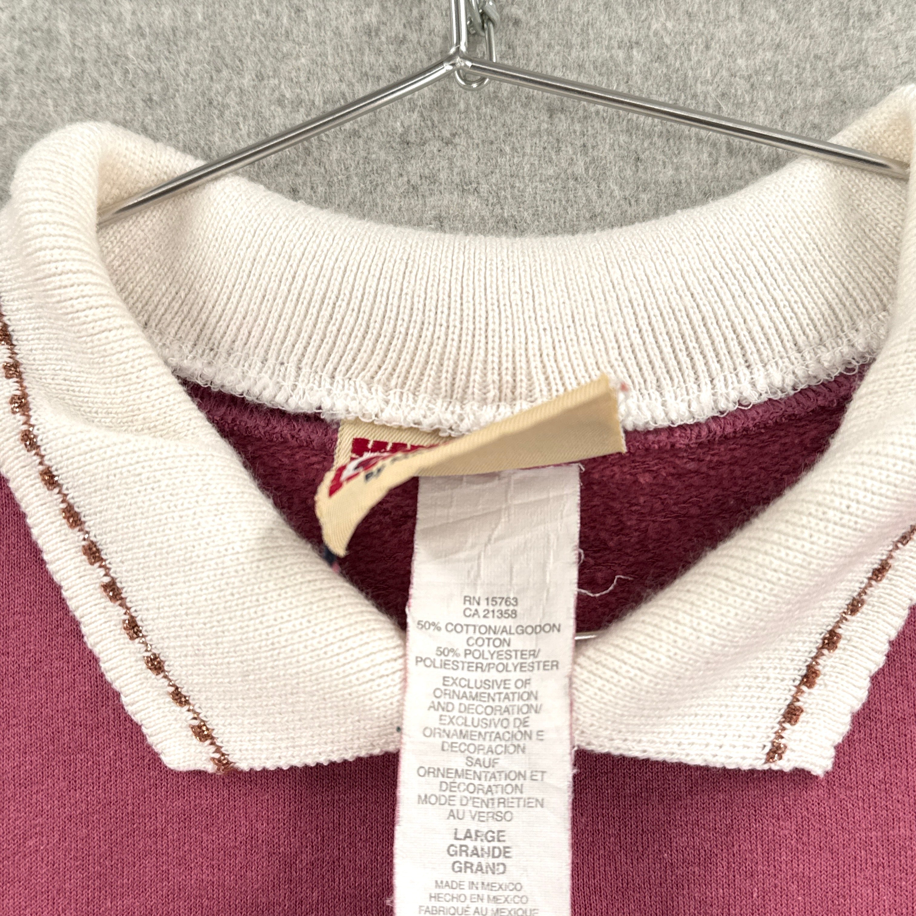 Close-up of a sweater with a brand tag on a hanger against a gray background. Size large 100% cotton