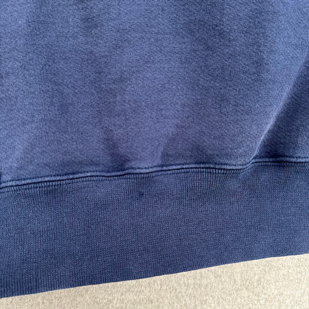 Close-up of a blue sweatshirt with a beige patch on a neutral background. back of sweatshirt small hole at the bottom hem