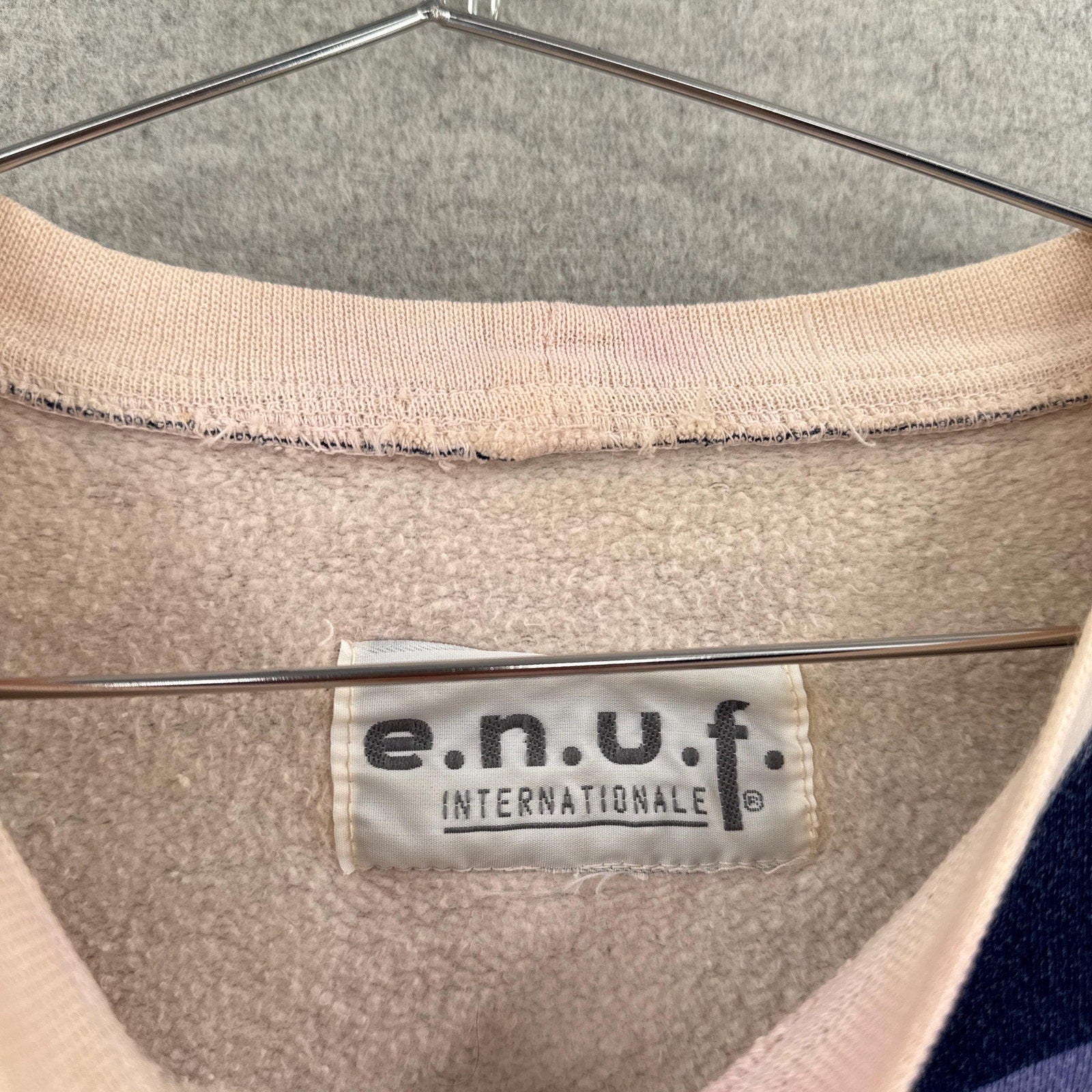 Close-up of a beige garment with an e.n.u.f. label on a hanger.
