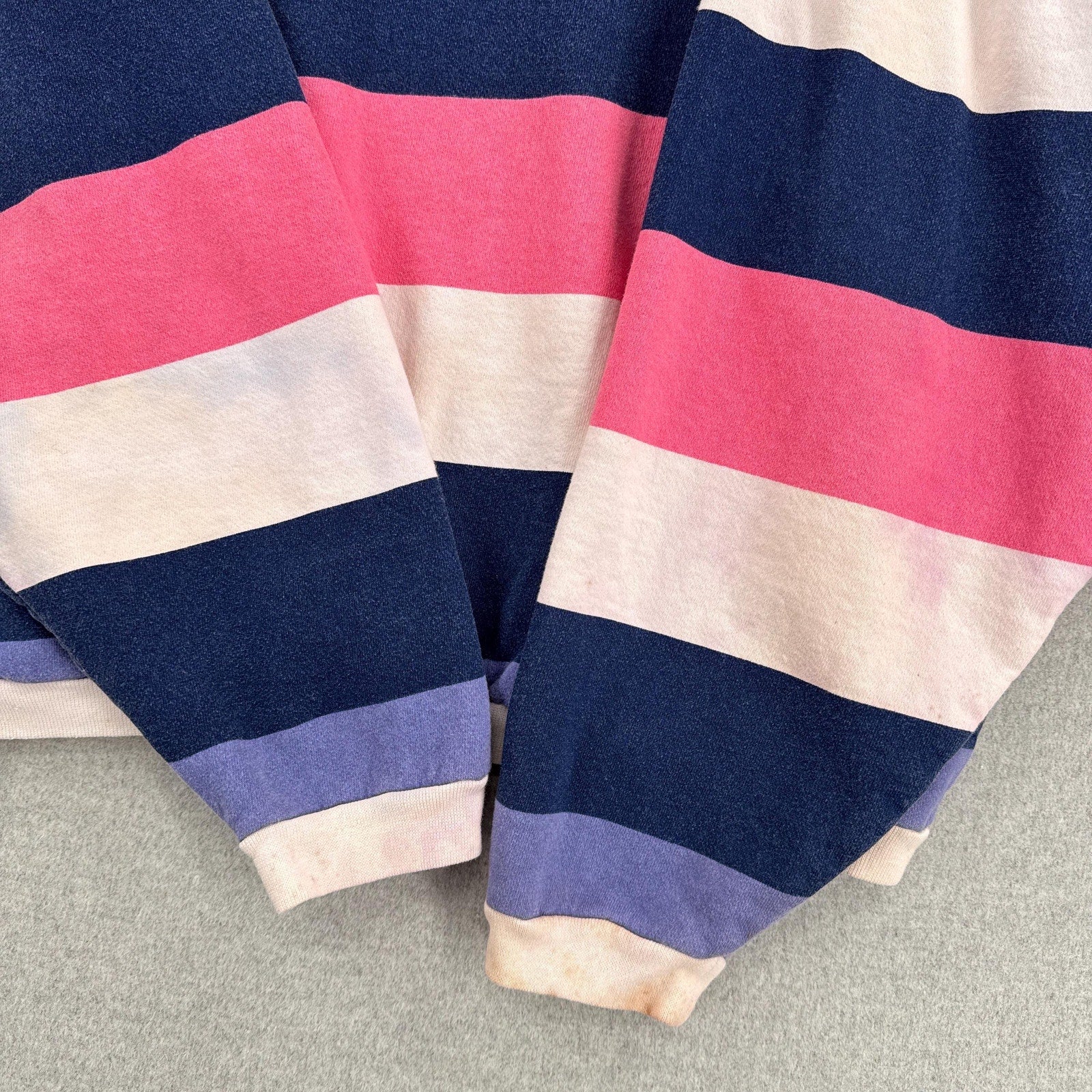 Close-up of a striped fabric with pink, blue, and beige colors on a gray surface.