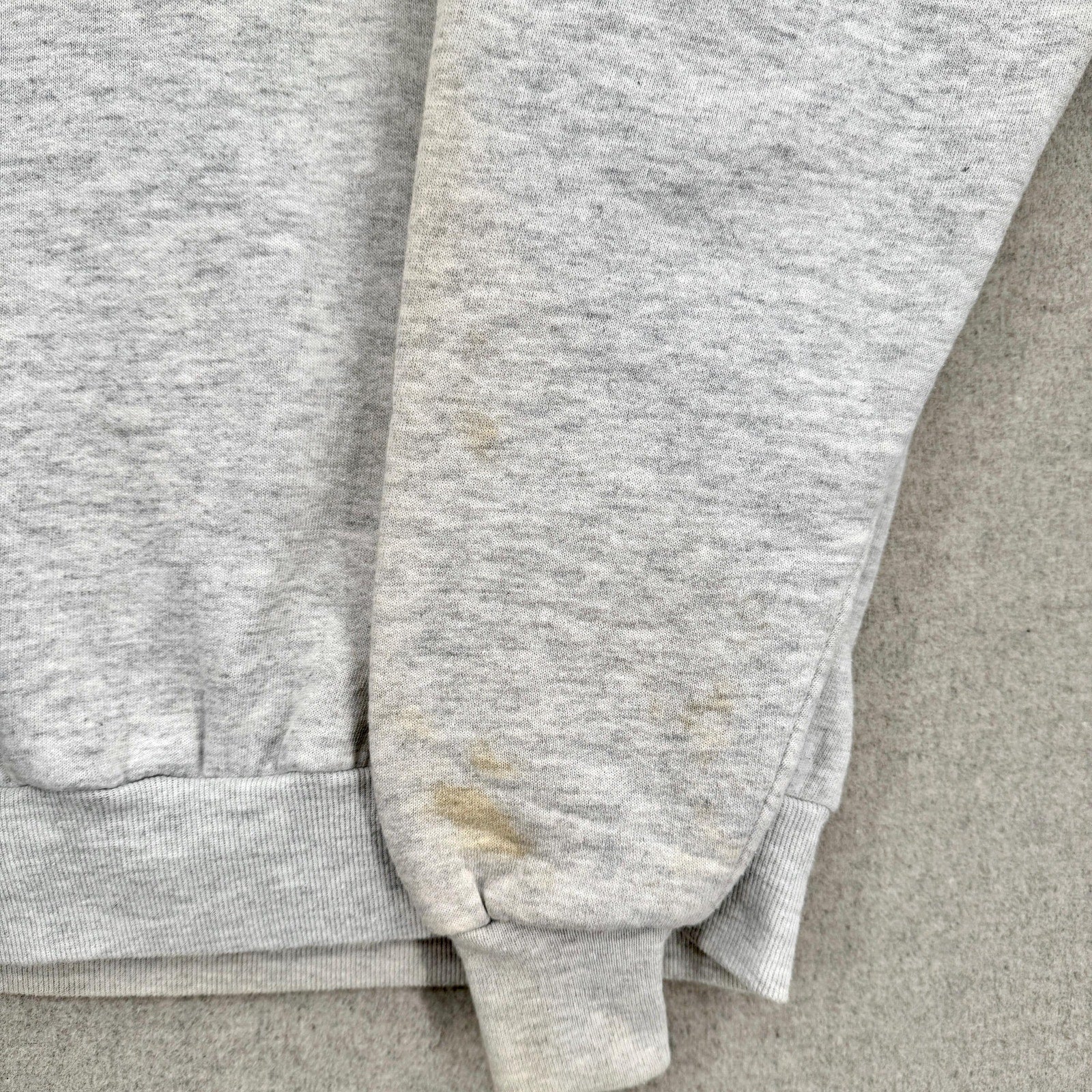 Gray sweatpants with visible stains on a gray surface, stains on sleeves