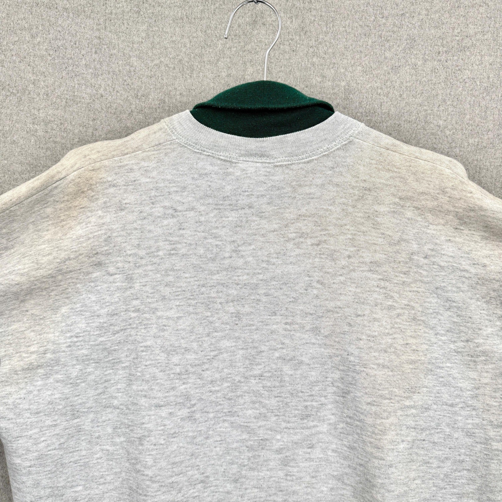 Gray sweatshirt on a hanger against a neutral background, discolouration around neckline