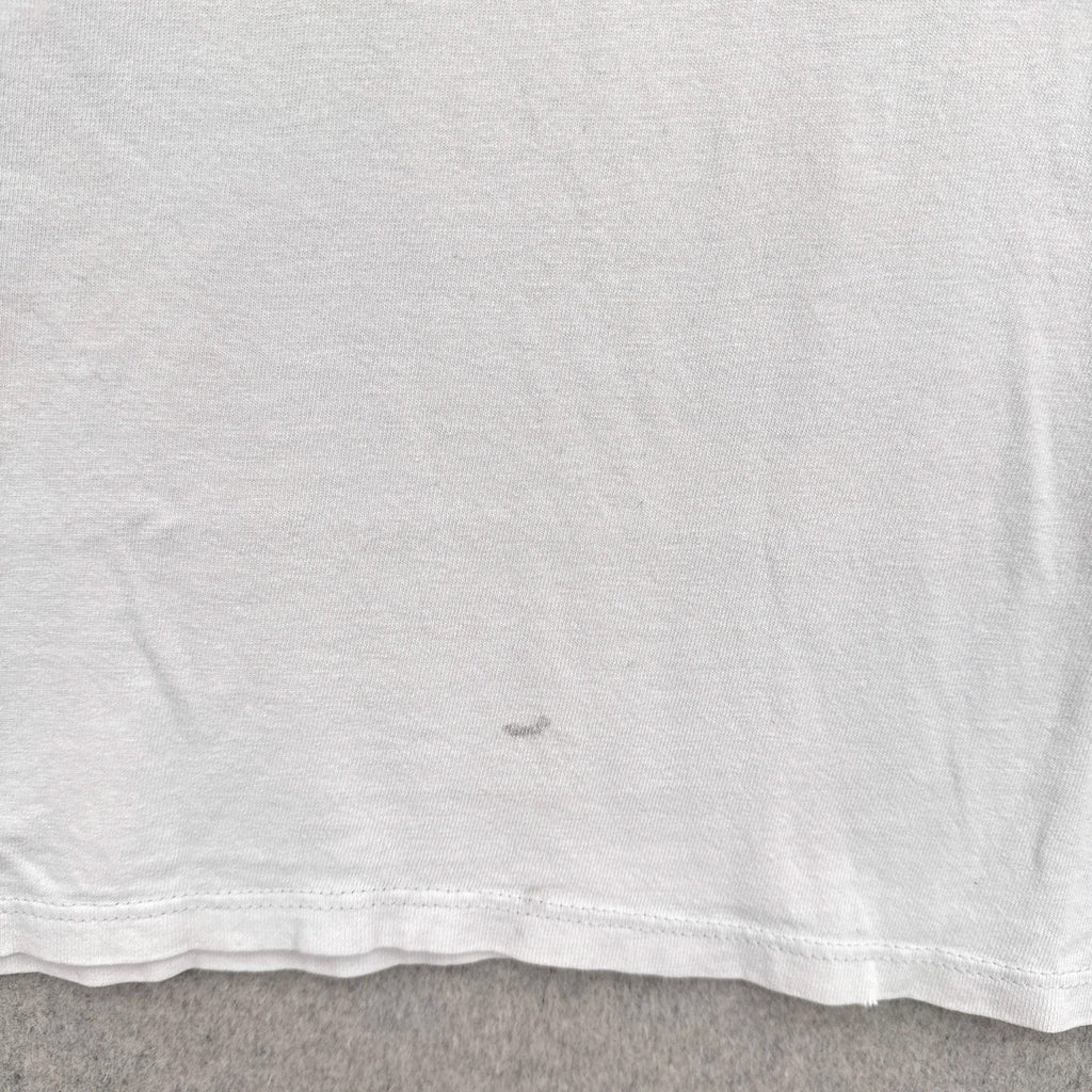 Close-up of a white t-shirt with a dark grey stain spot on a gray surface