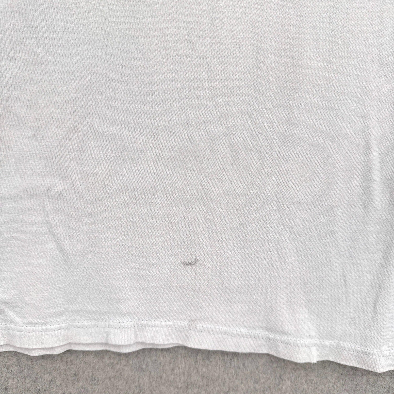 Close-up of a white t-shirt with a dark grey stain spot on a gray surface