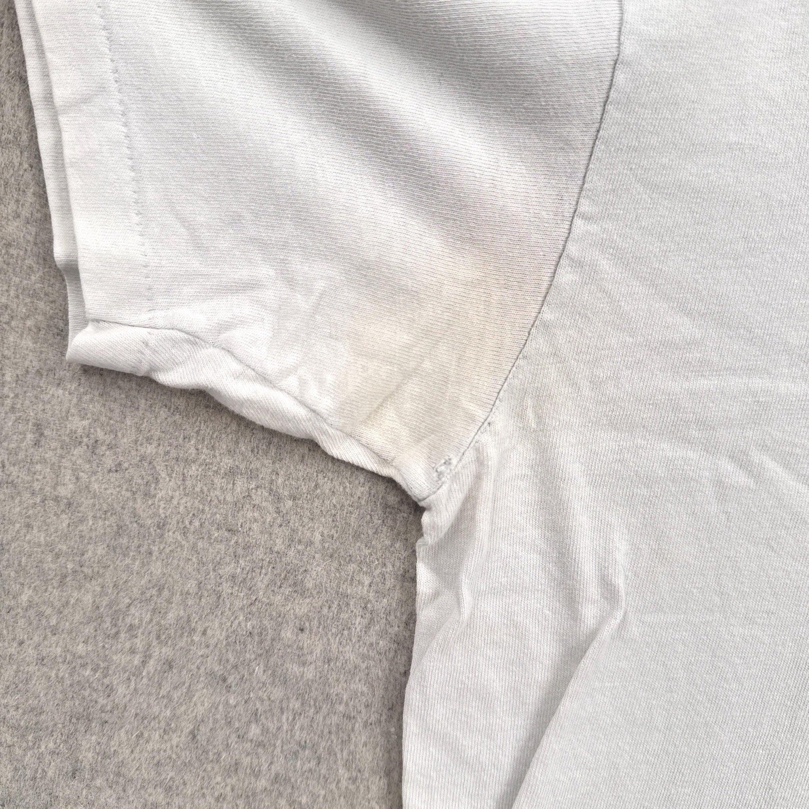 Close-up of a white shirt collar on a textured gray surface. discolouration and hole around armpit