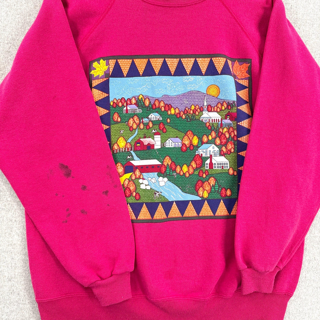 Pink sweatshirt with a colorful graphic of a village scene on a light gray background. stain spot on sleeve
