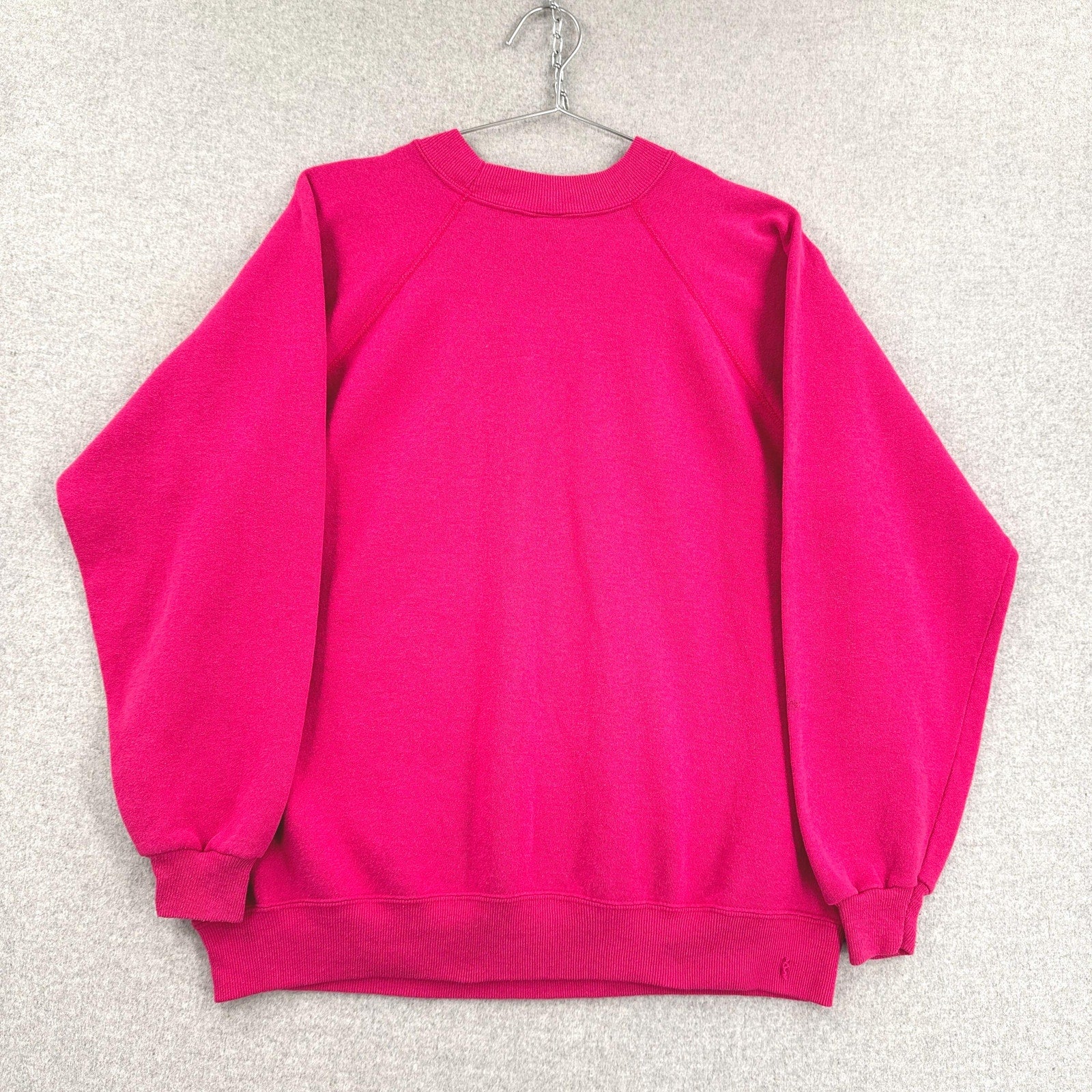 Hot pink sweatshirt on a hanger against a textured white background
