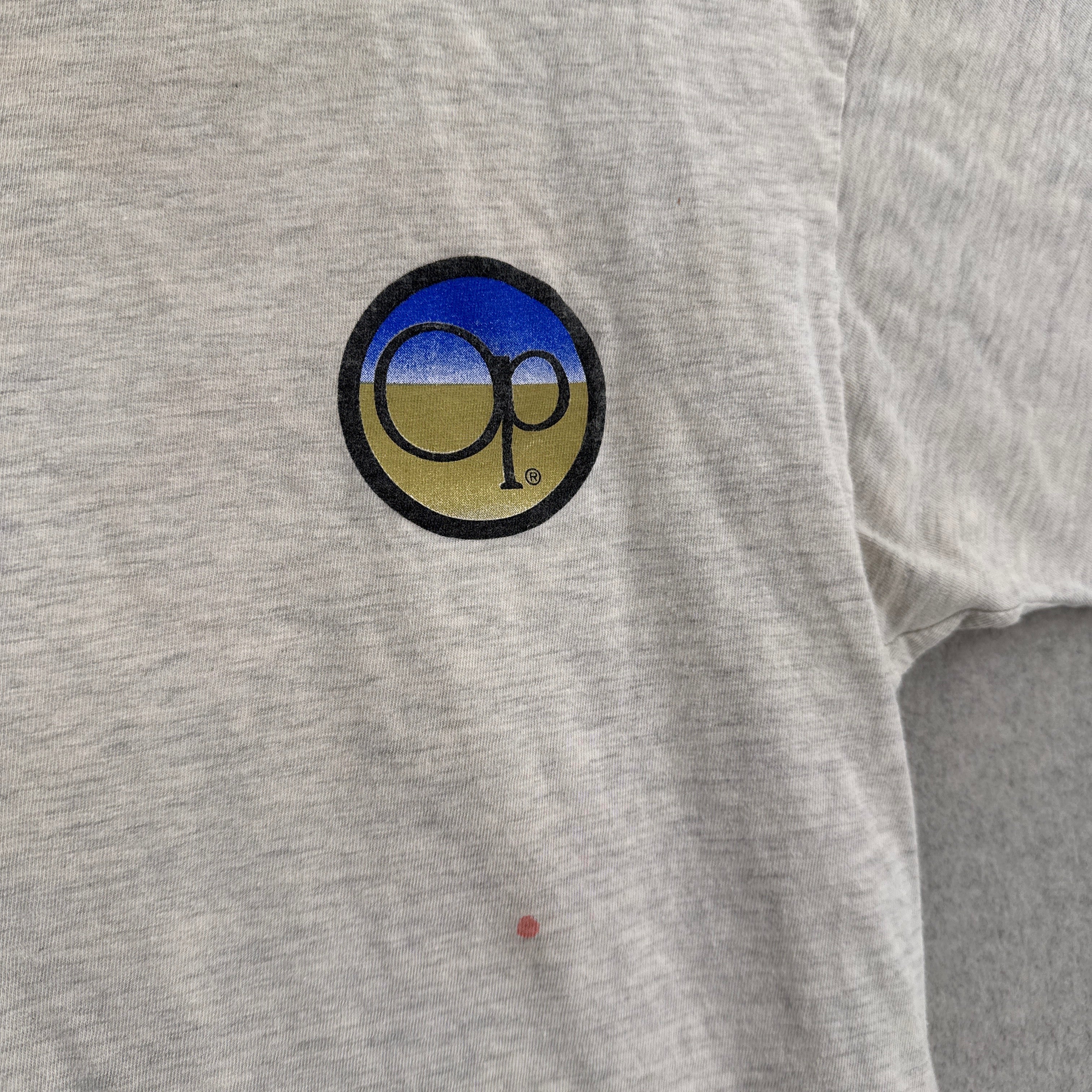 Close-up of a gray shirt with a logo on the chest. OP logo in a circle with a stain spot under it