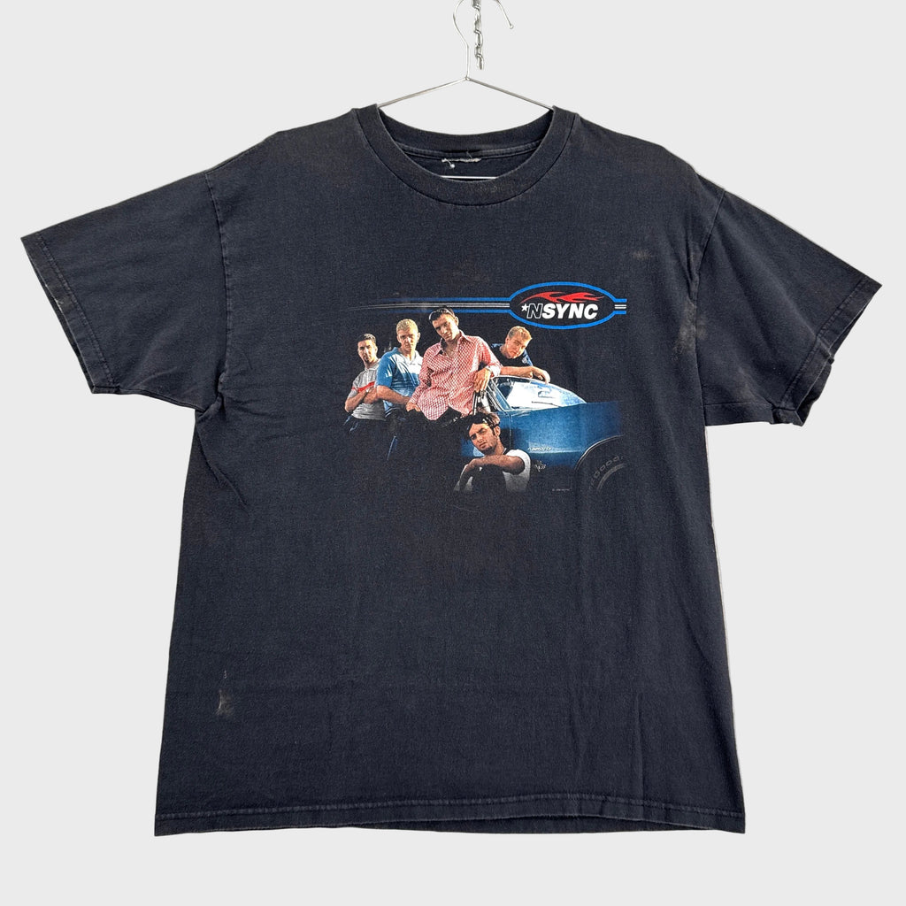 Black t-shirt with graphic design of a boy band NSYNC, hanging on a gray textured surface.