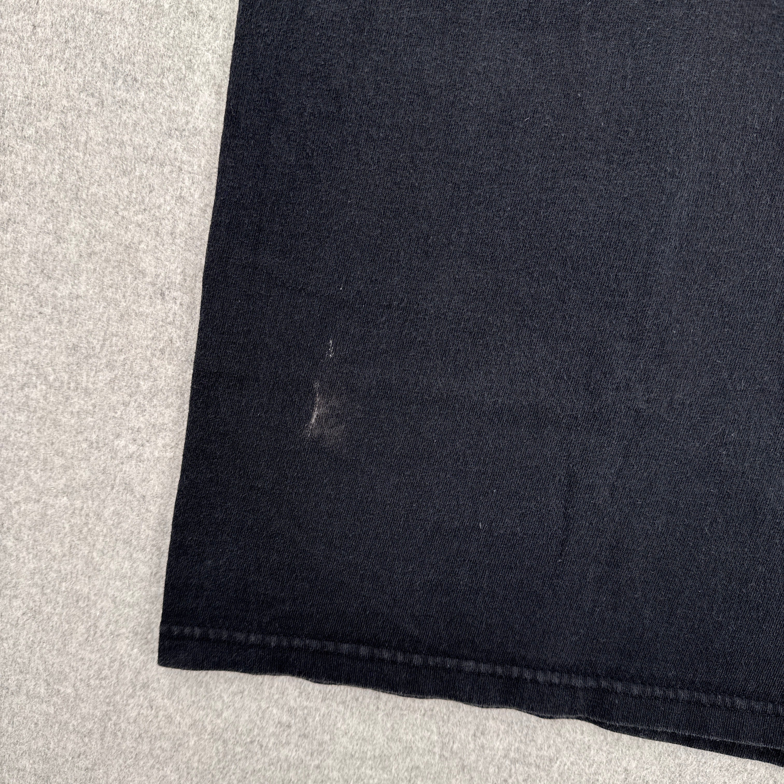 Close-up of a black fabric edge on a light gray background. stain spot near bottom edge