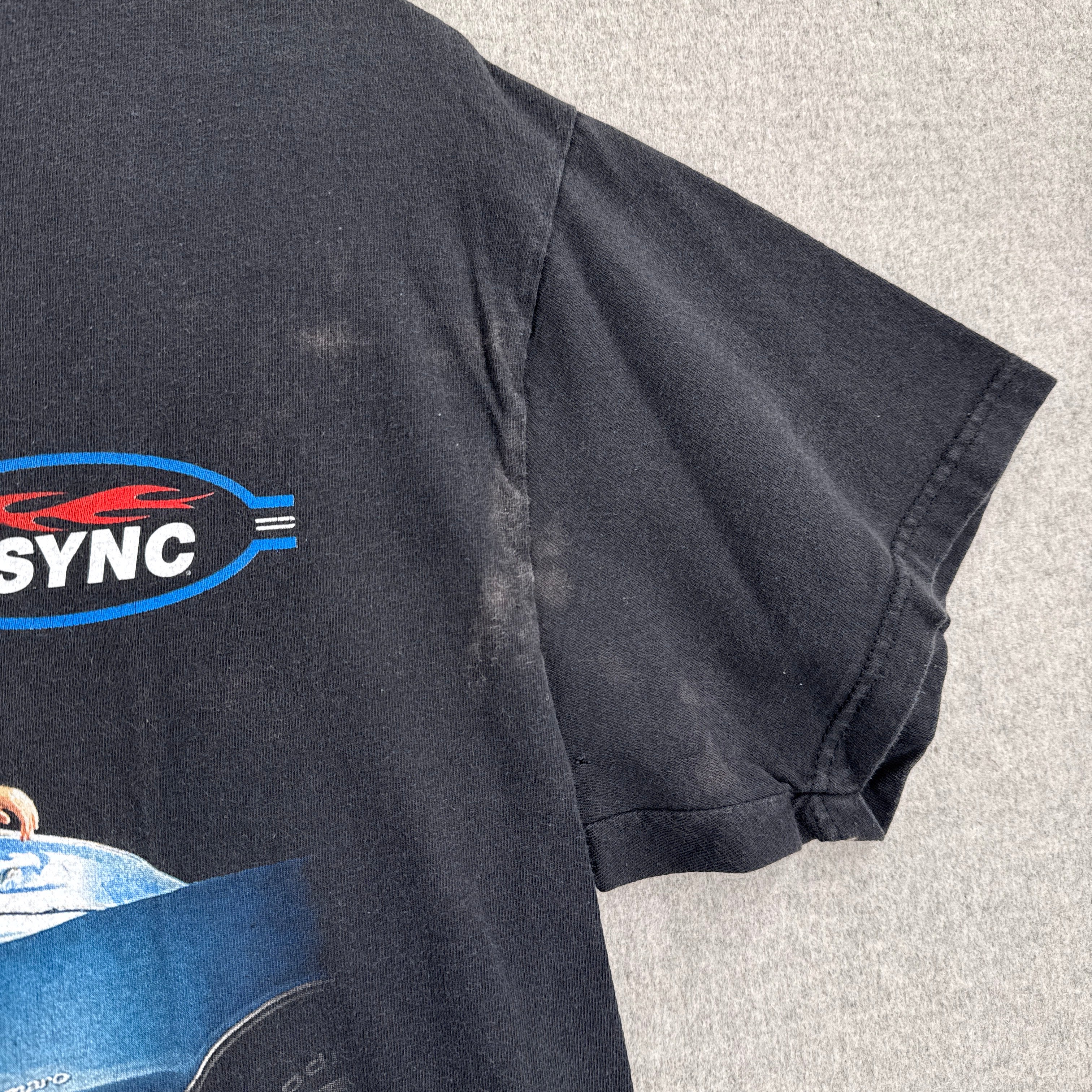 Black shirt with a logo on a gray surface, stain spots near armpit