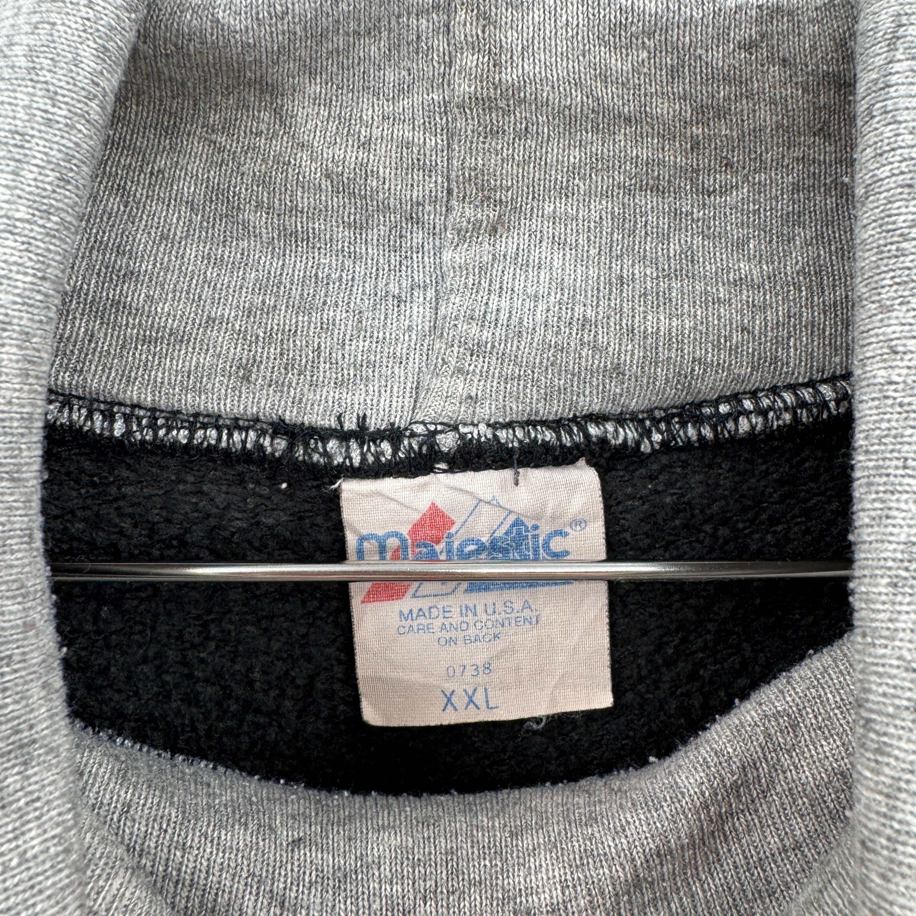 Close-up of a Majestic label on a gray sweatshirt with black trim. Size XXL make in USA