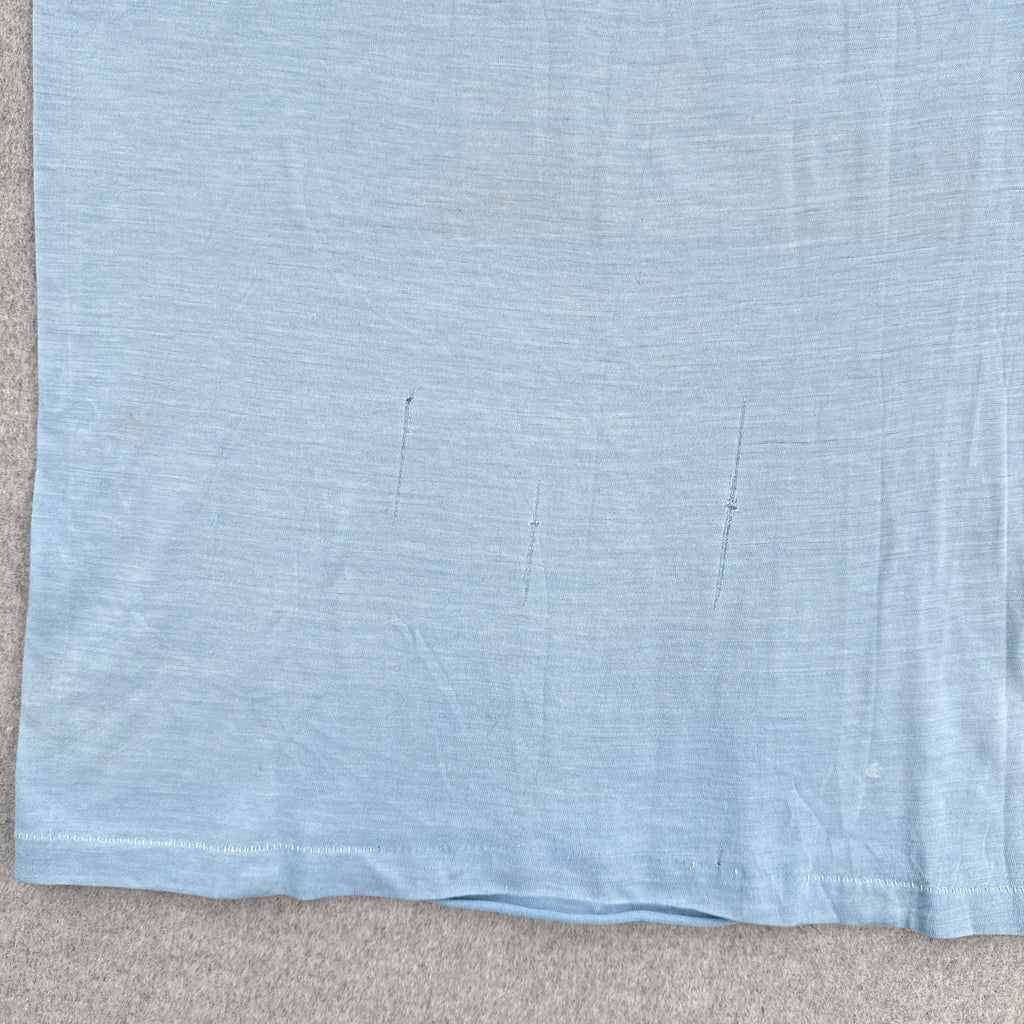Light blue fabric with a subtle pattern on a beige surface. Runs in the fabric