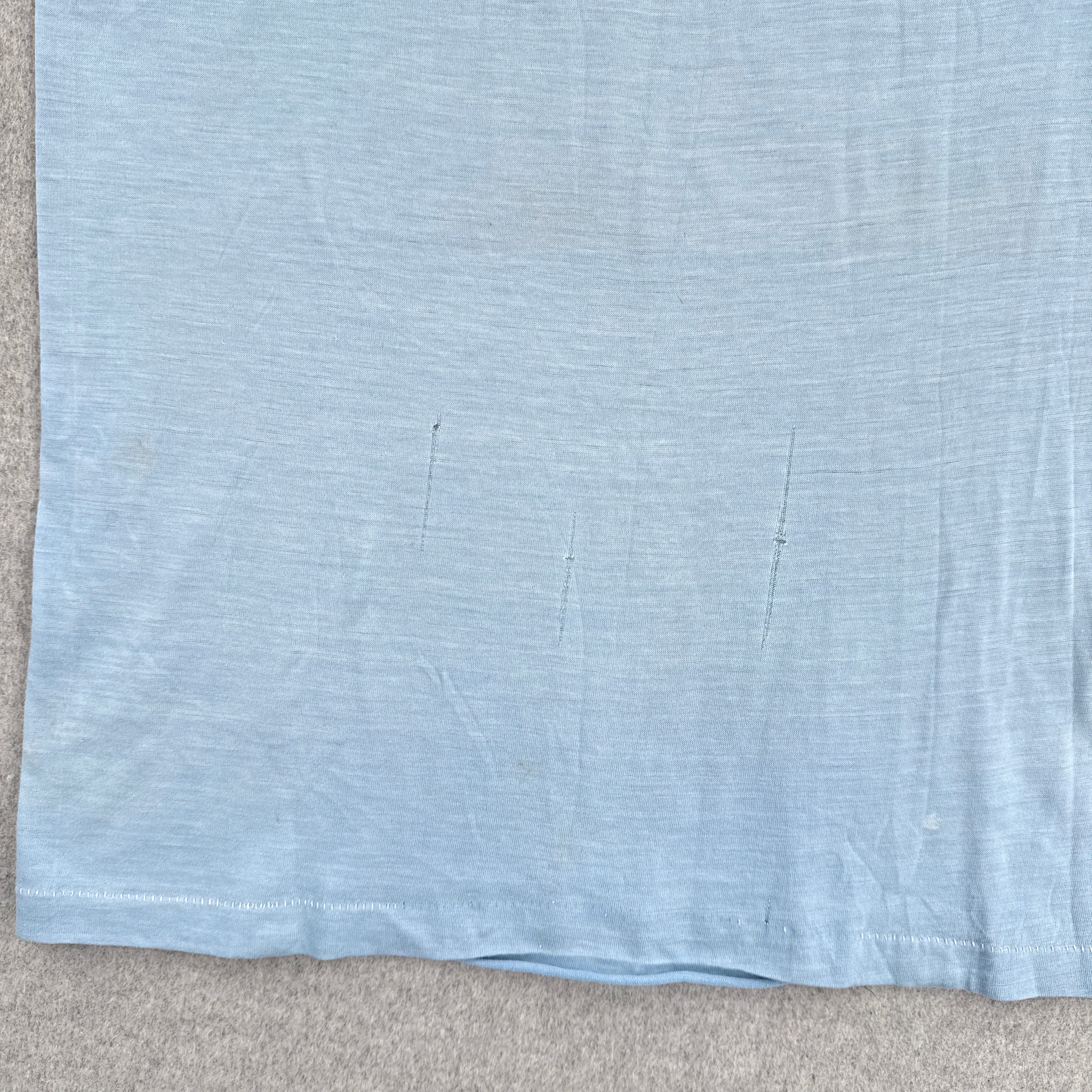 Light blue fabric with a subtle pattern on a beige surface. Runs in the fabric