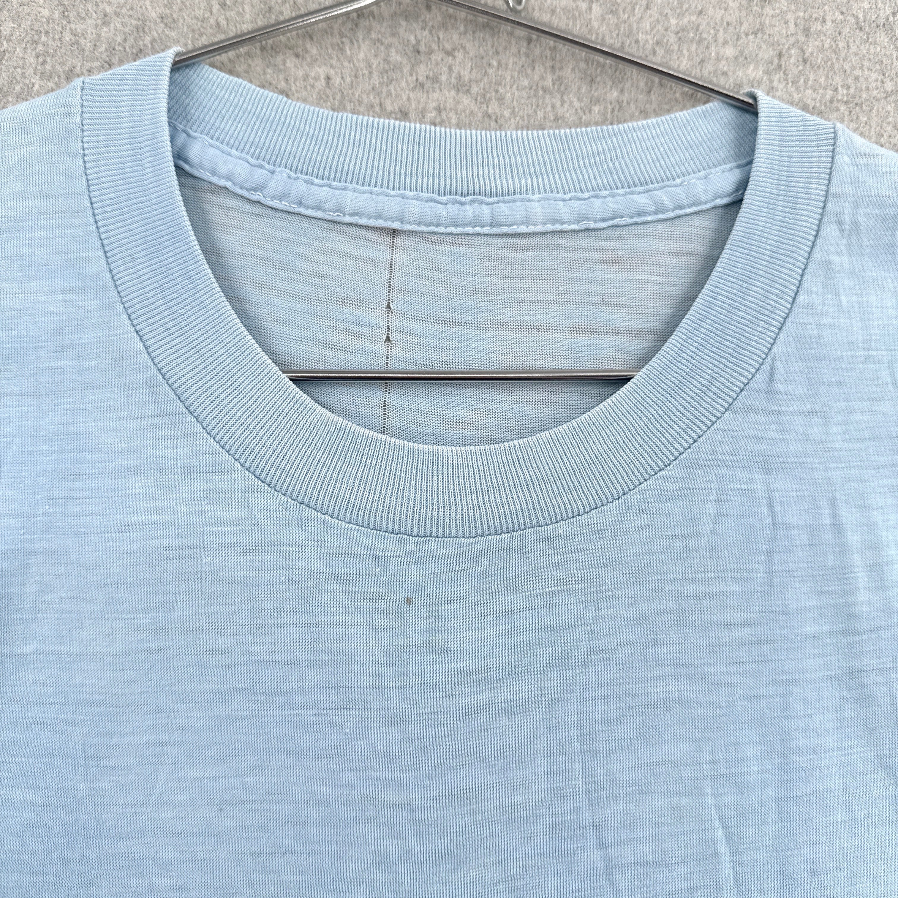 Light blue t-shirt on a hanger against a neutral background. No tag, small stain spot around collar