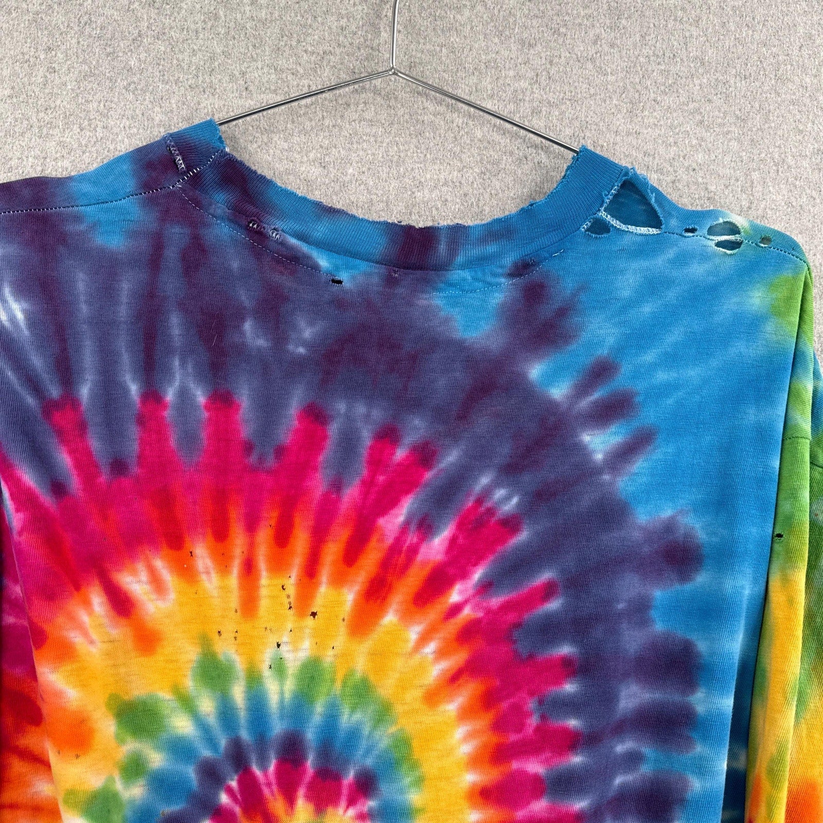 Tie-dye shirt with a colorful spiral pattern on a hanger against a neutral background