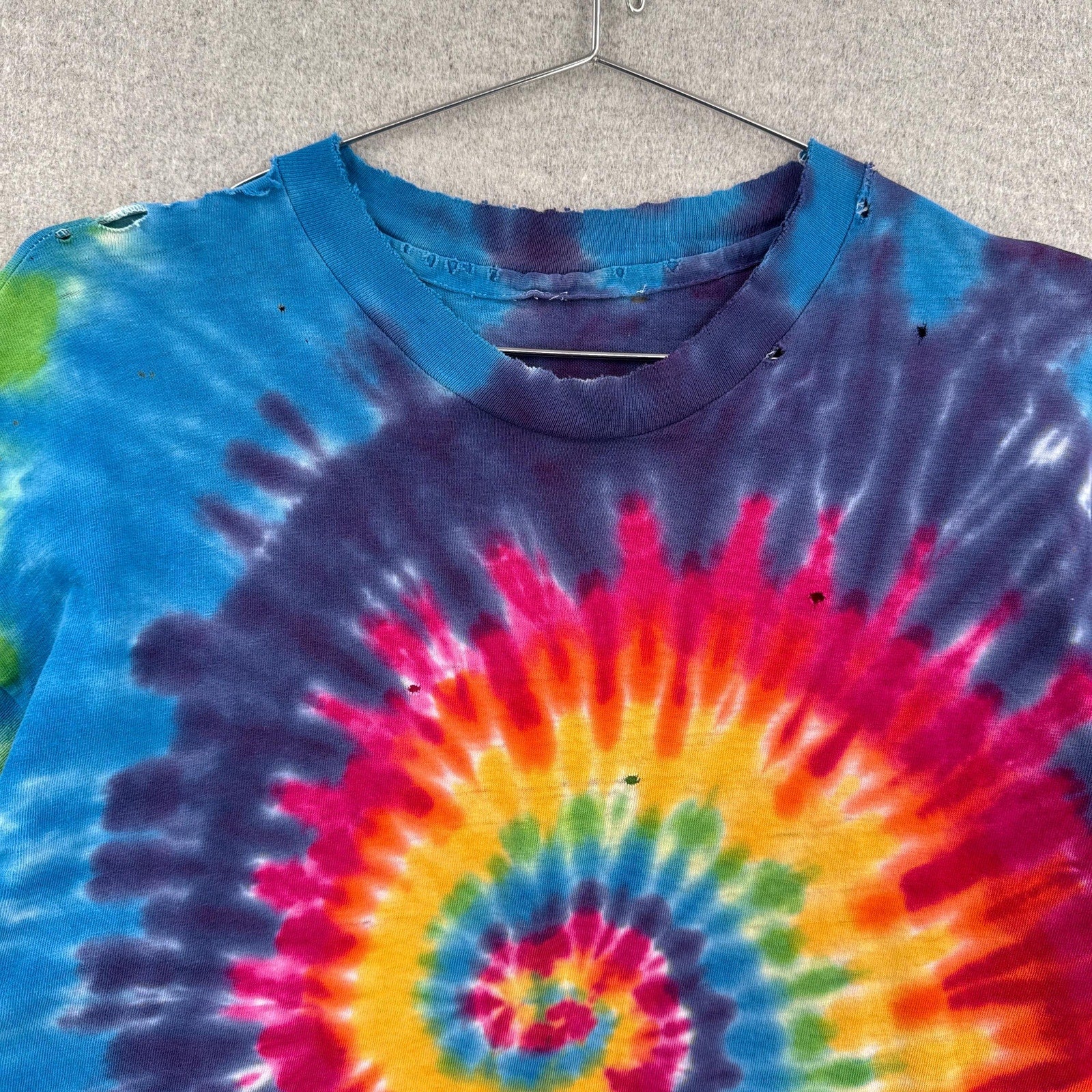 Tie-dye t-shirt with a spiral pattern on a hanger against a neutral background