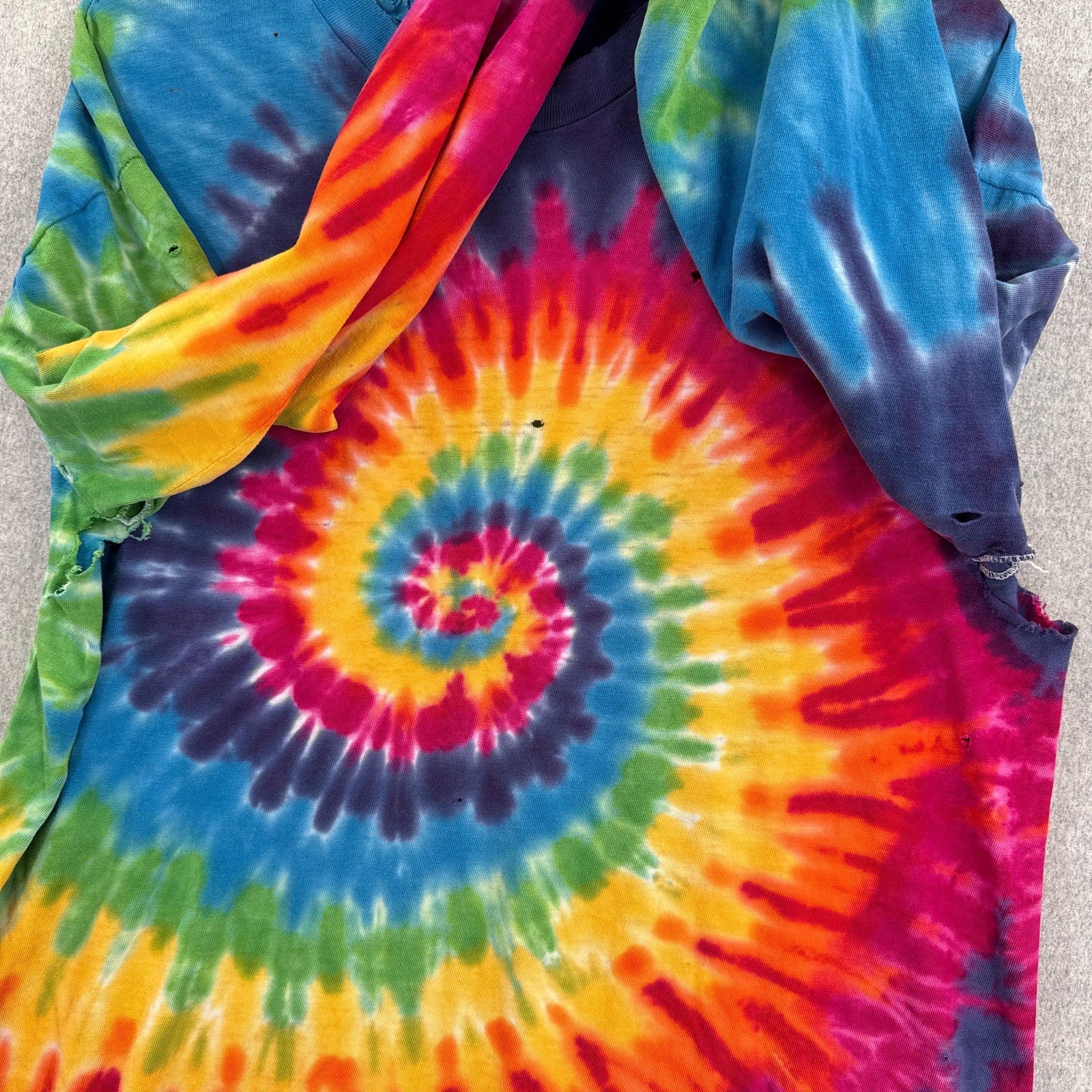 Close-up of a tie-dye shirt with a multicolor spiral pattern on a neutral background.
