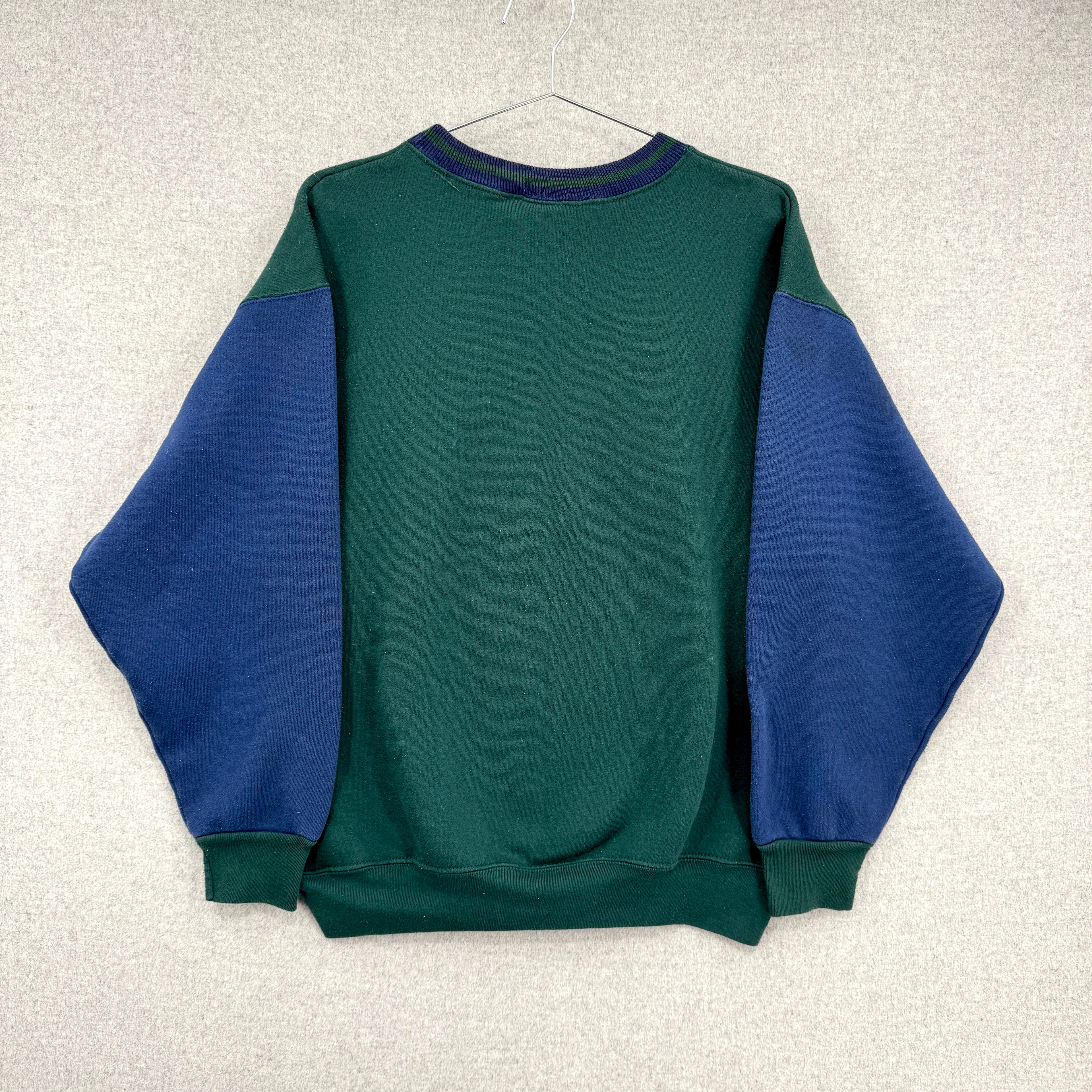 Green and blue sweatshirt on a hanger against a light gray background