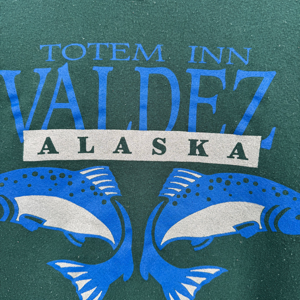 Logo of Totem Inn Valdez Alaska with blue fish illustrations on a green background