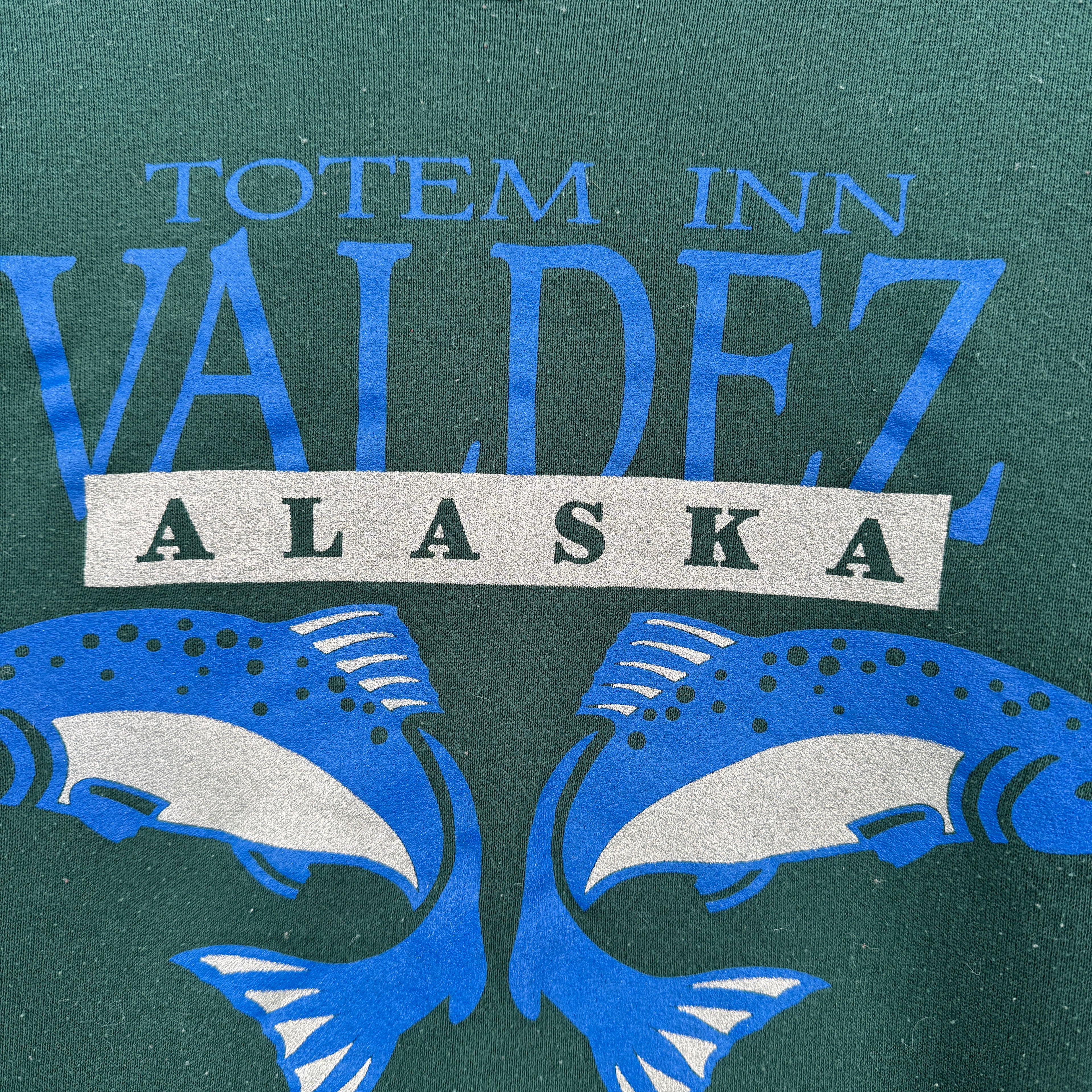 Logo of Totem Inn Valdez Alaska with blue fish illustrations on a green background