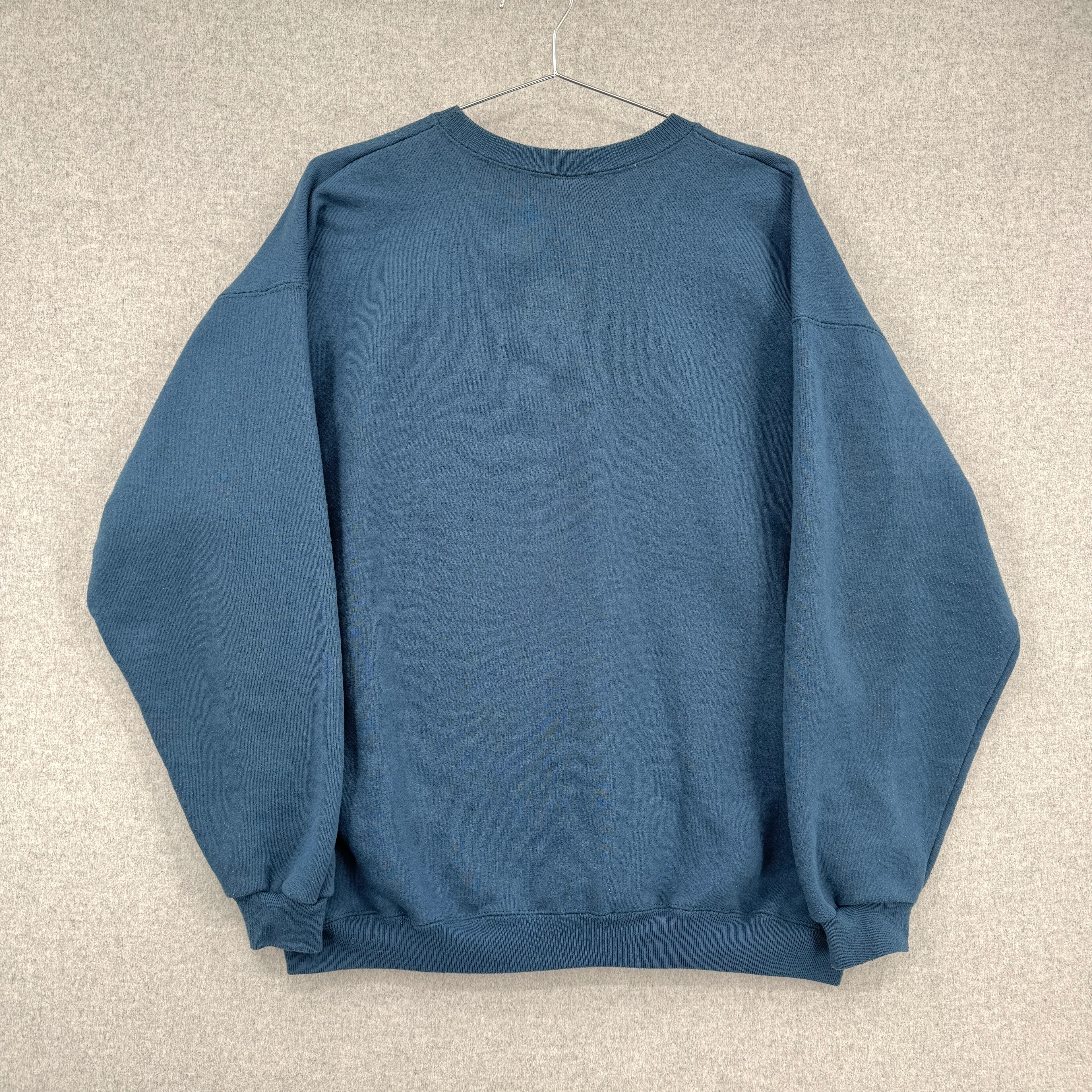 back of blue sweatshirt on a hanger against a beige wall