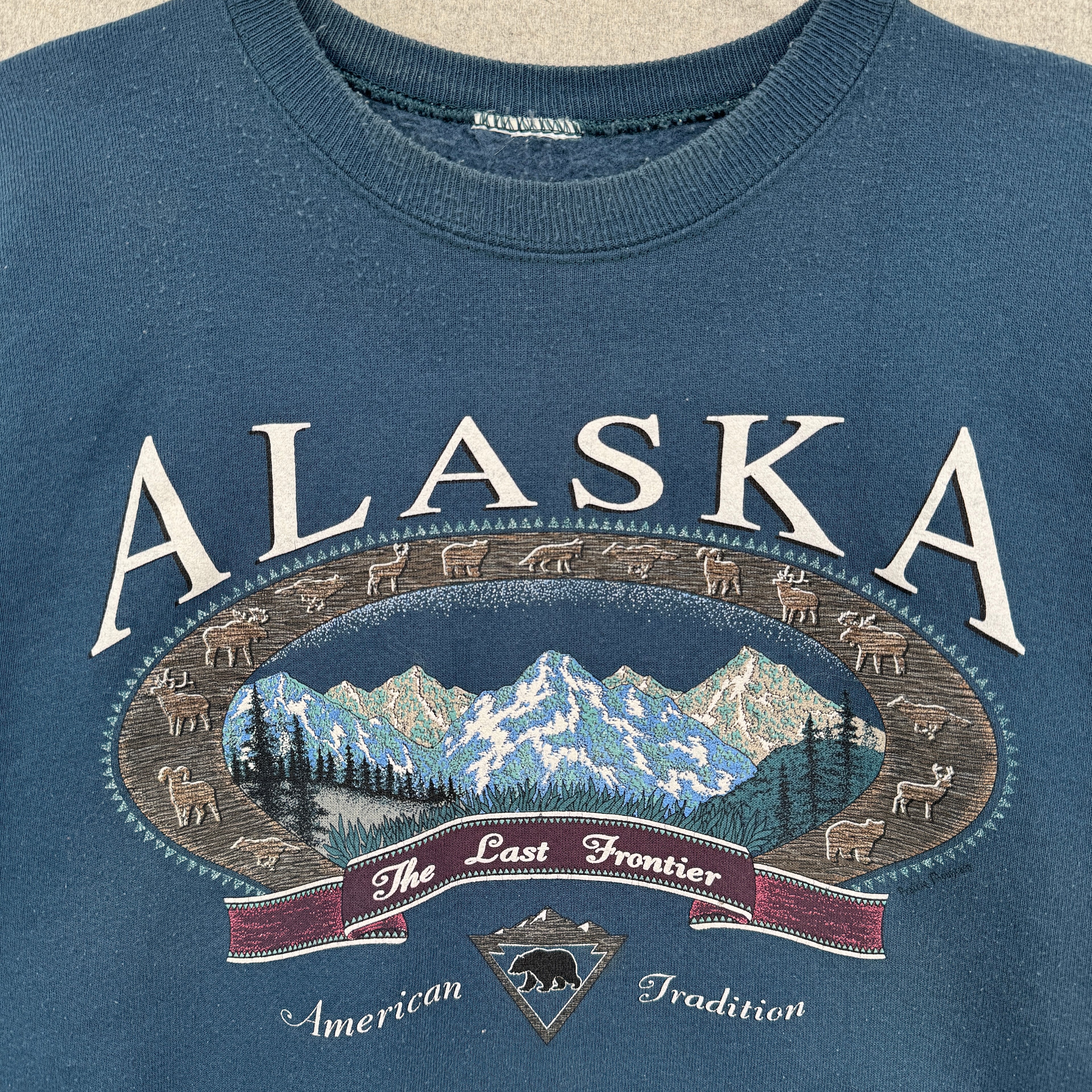 Blue sweatshirt with 'Alaska The Last Frontier American Tradition' graphic design. Mountains and animals