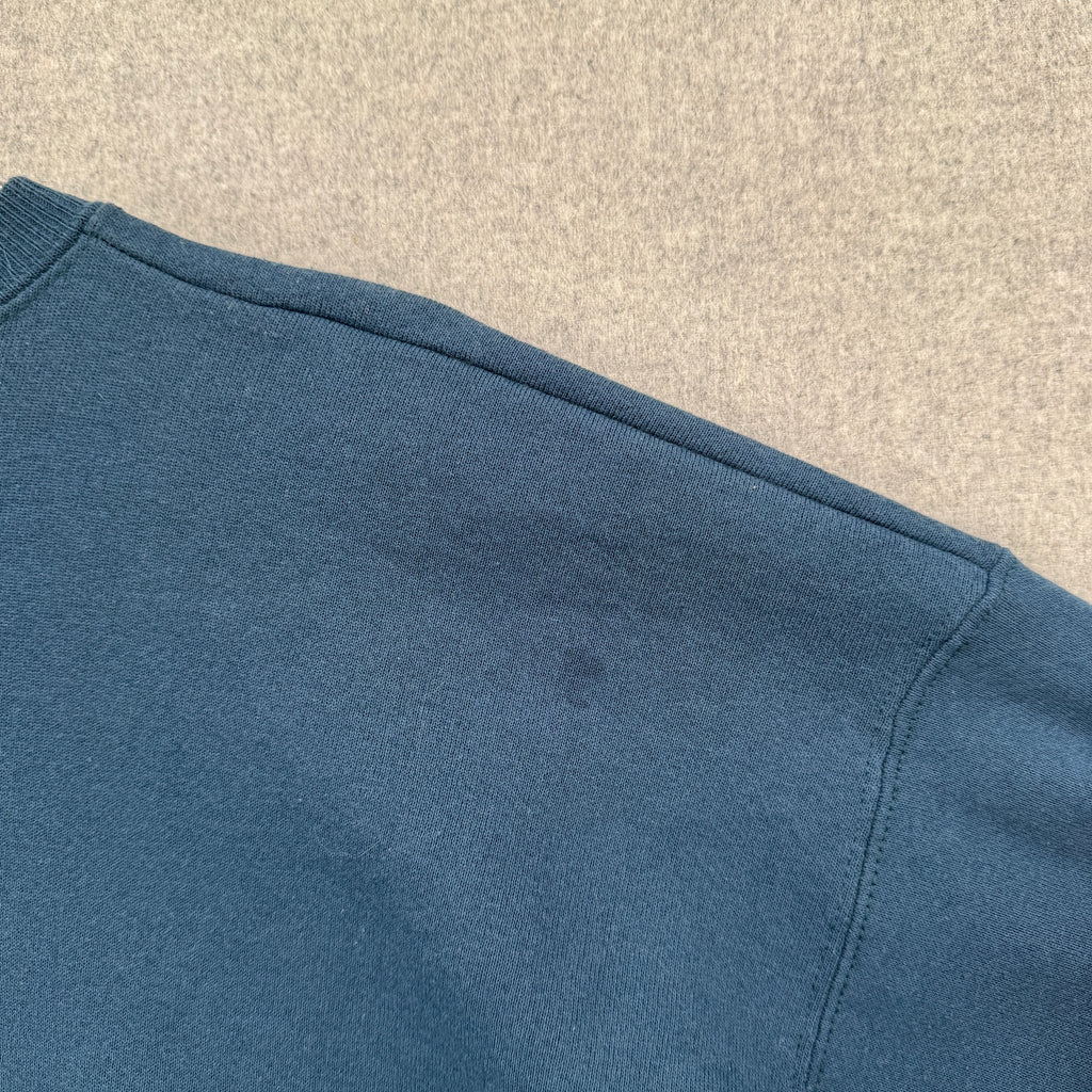 Close-up of a blue fabric texture on a beige background, small stain spot near shoulder on back of sweatshirt