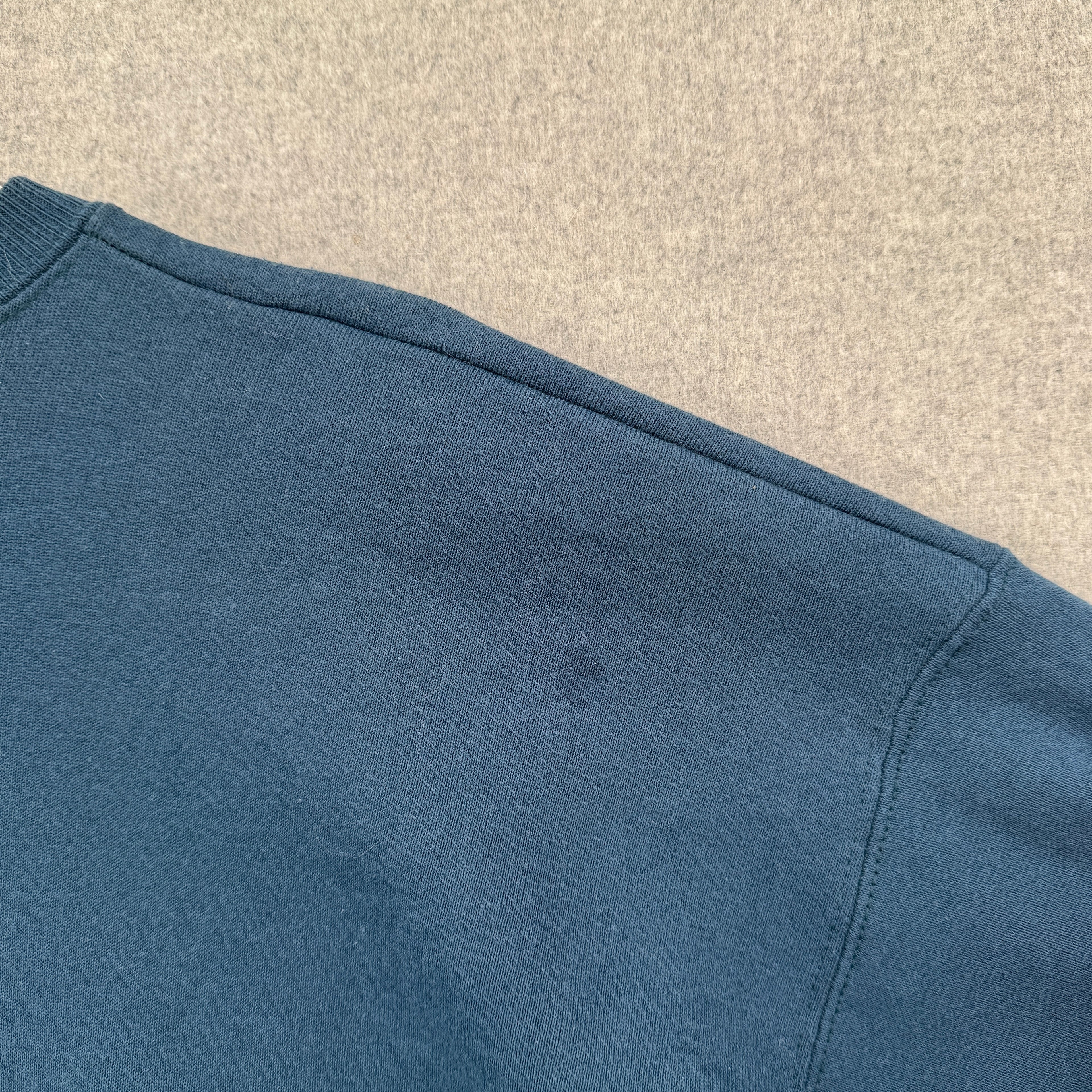 Close-up of a blue fabric texture on a beige background, small stain spot near shoulder on back of sweatshirt
