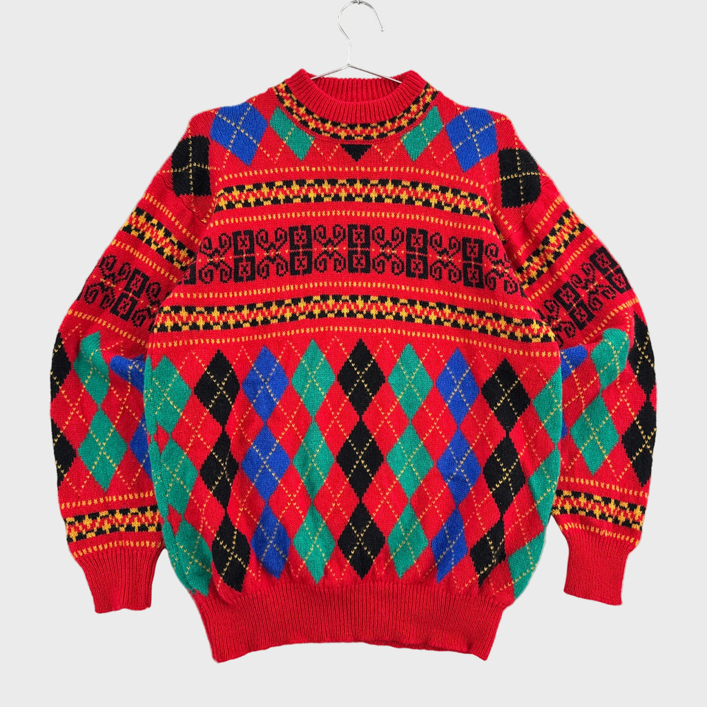 A red knit sweater with a colorful argyle and geometric pattern, hanging on a clear hanger against a light gray textured background.