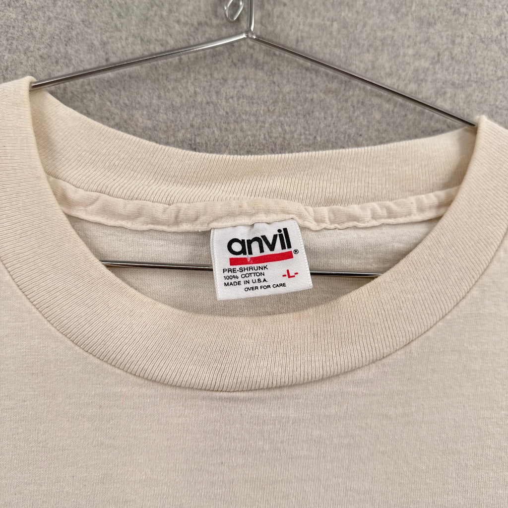 Close-up of a beige shirt with a brand label on a neutral background. Anvil tag size Large made in USA 100% cotton
