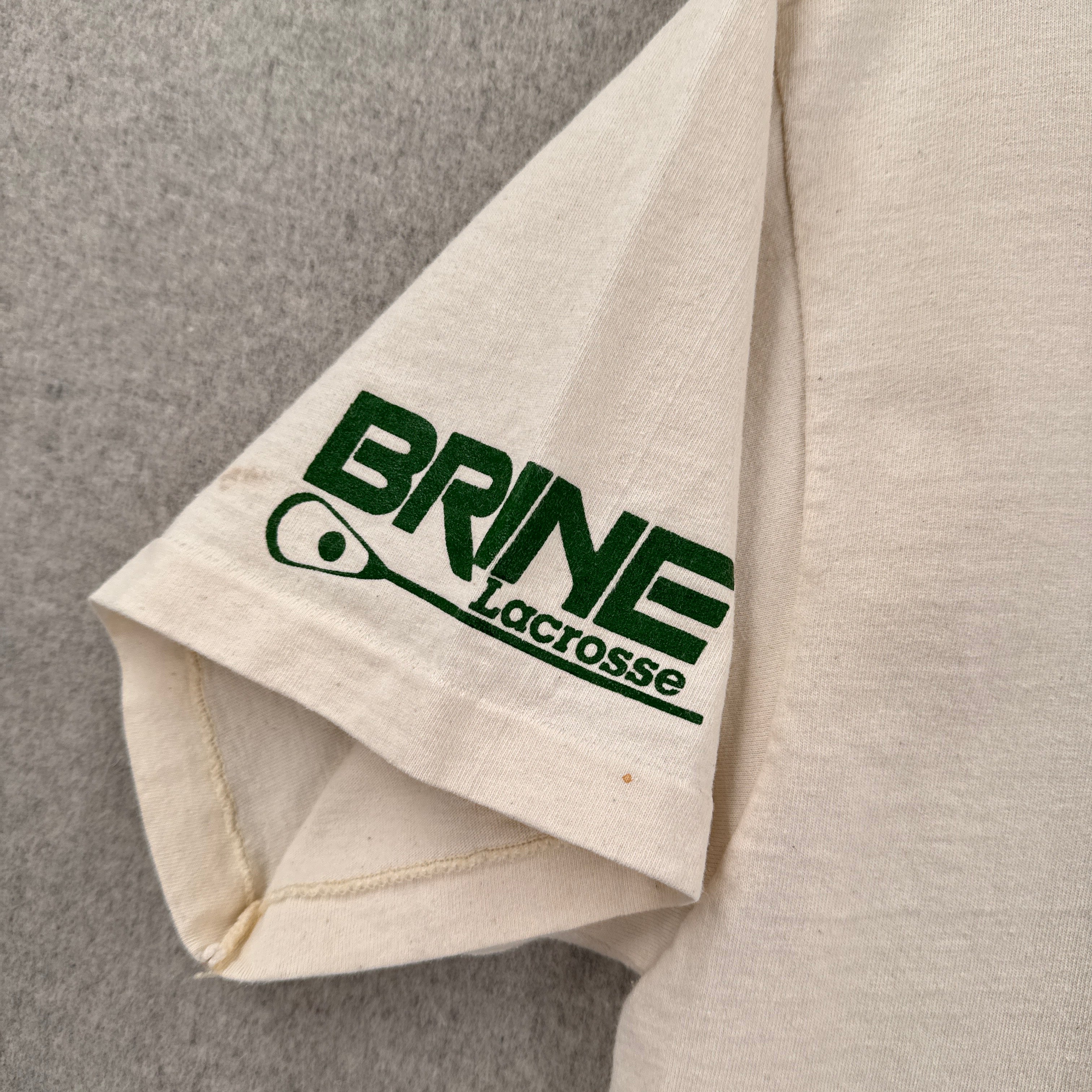 Beige sleeve with green 'Brine Lacrosse' logo on a gray background