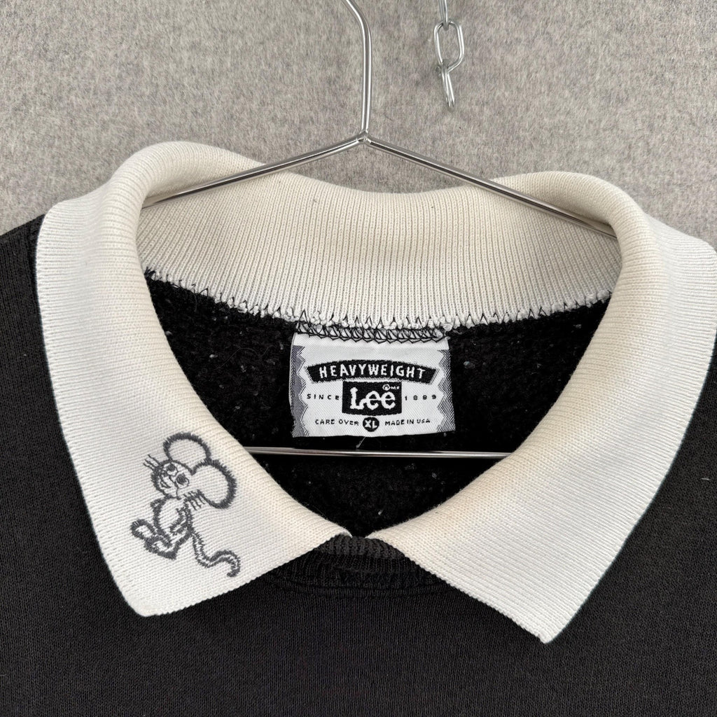 Black sweater with white collar and embroidered design on a hanger against a gray background