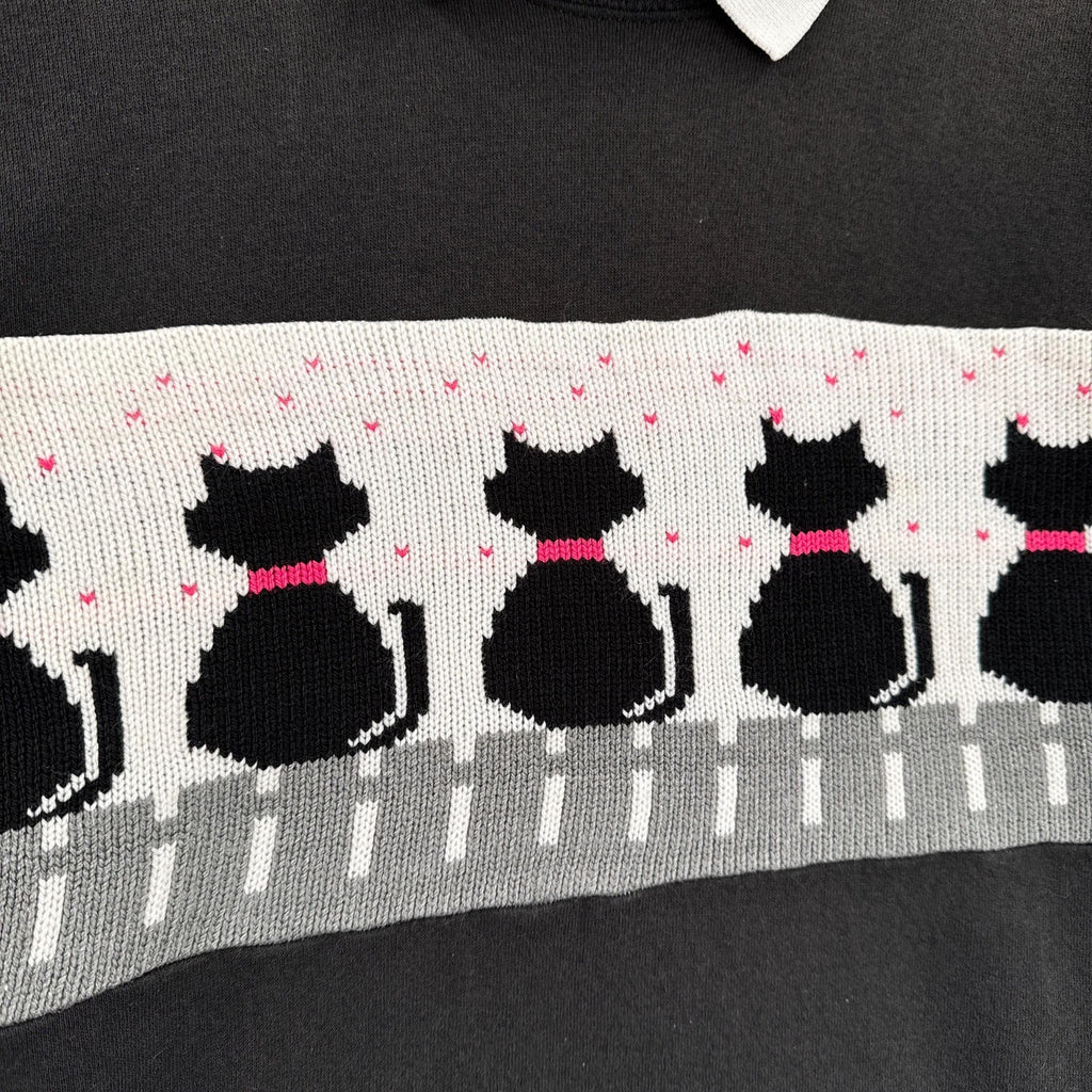 Black sweater with a pattern of black cats and pink bows on a gray background