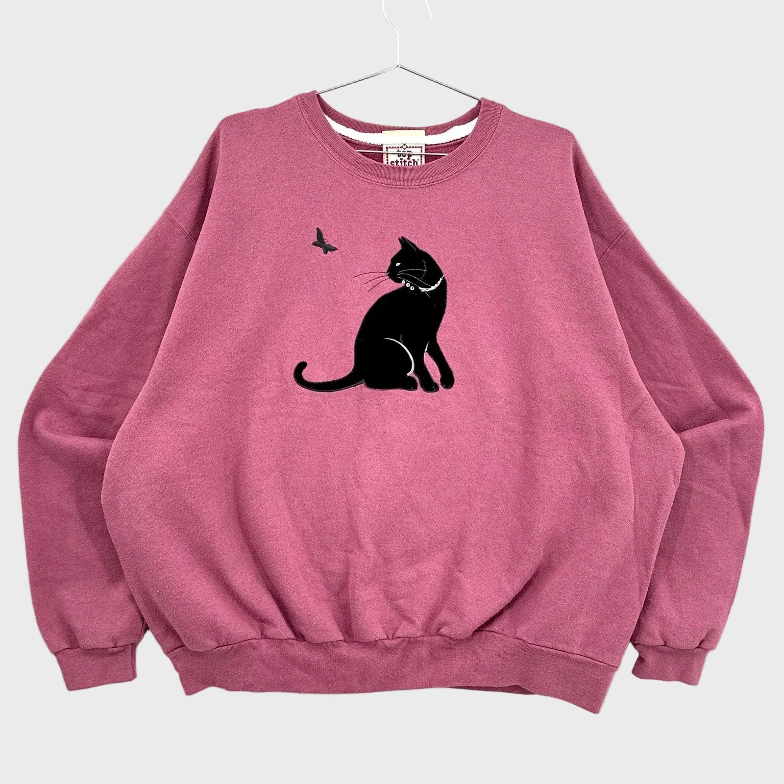 Pink sweatshirt with a black cat and butterfly design on a gray background