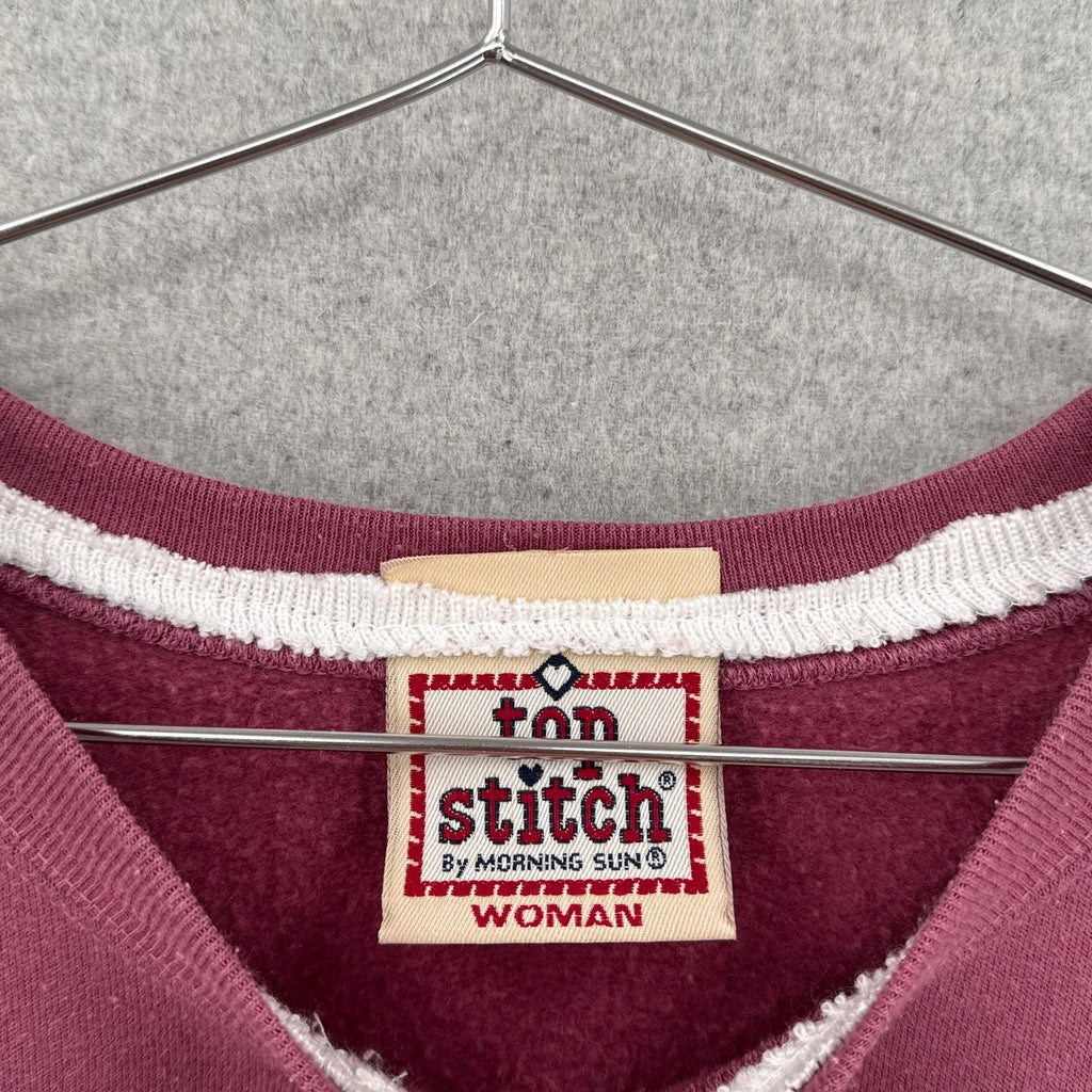 pink sweatshirt with 'top stitch' label on a hanger by morning sun