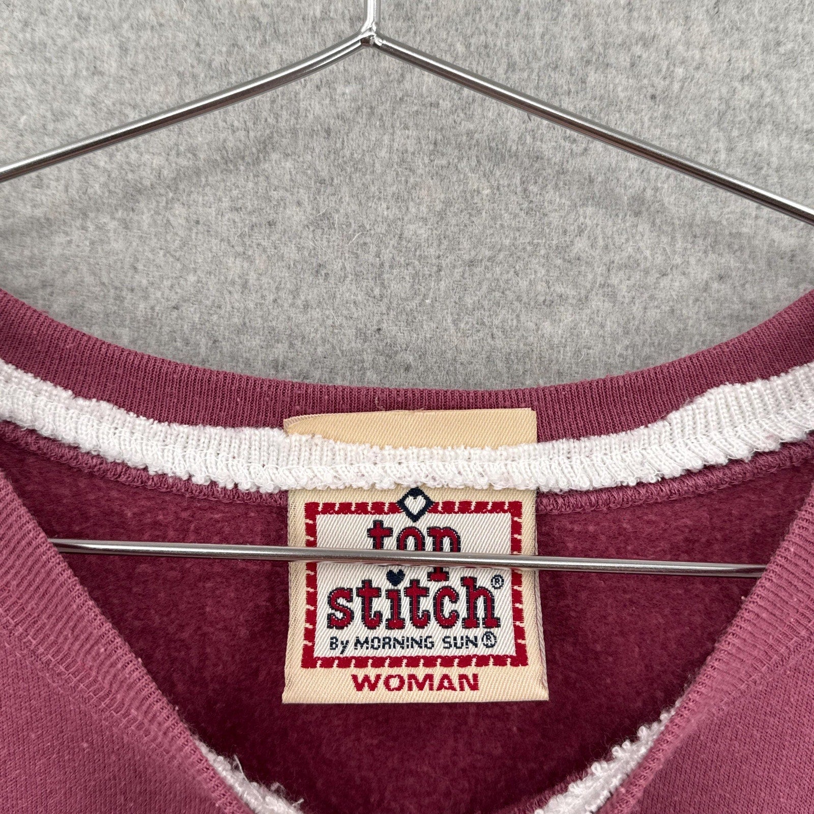 pink sweatshirt with 'top stitch' label on a hanger by morning sun