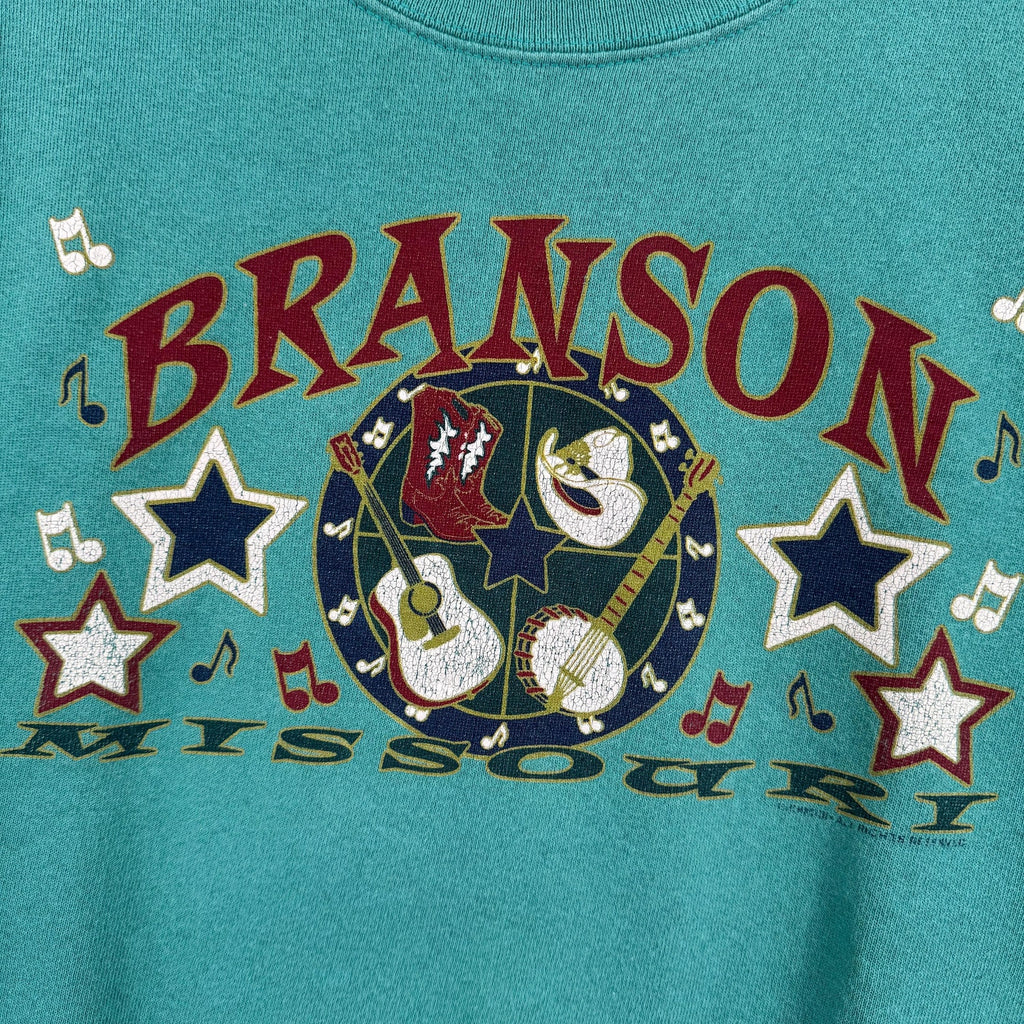 Teal t-shirt with 'Branson Missouri' text and musical design on a blue background