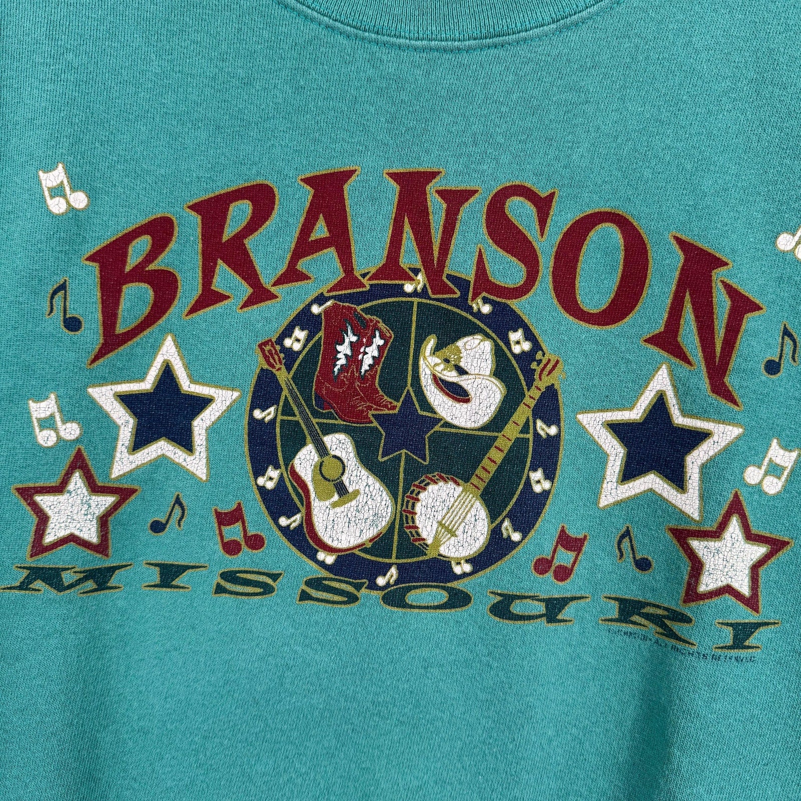 Teal t-shirt with 'Branson Missouri' text and musical design on a blue background